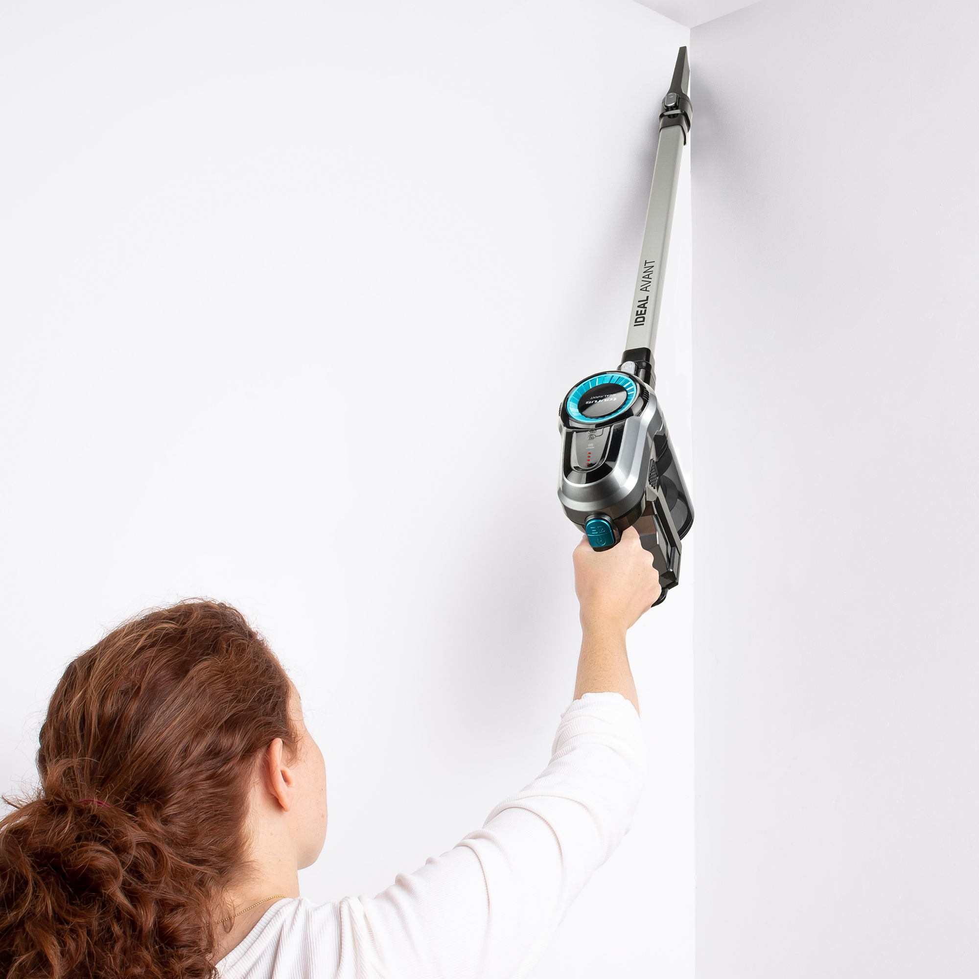 Donna che tiene un aspirapolvere per pulire un angolo del muro. Muro bianco, dispositivo argento e nero.