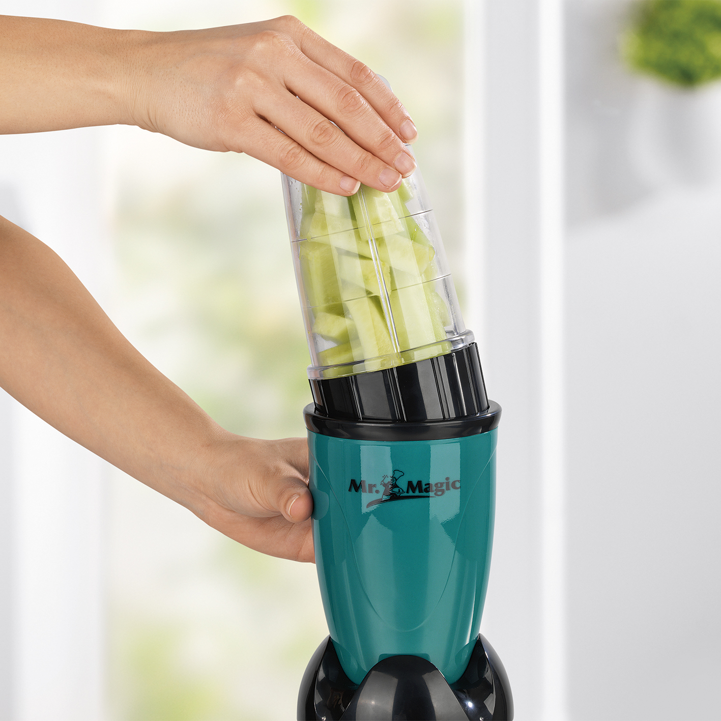 Una persona sta aggiungendo cetrioli tritati in un frullatore Mr. Magic verde acqua e nero.