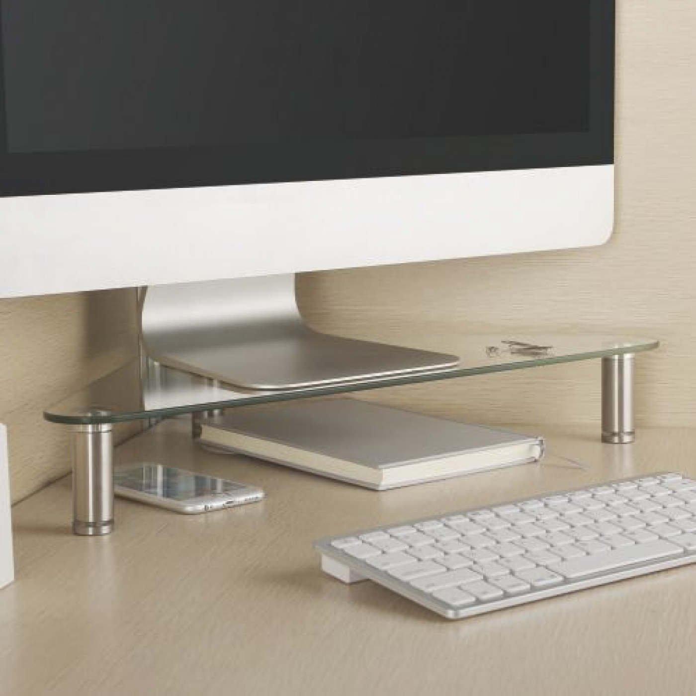 Ein Computermonitor auf einem Glasregal, mit Notizbuch und Telefon.
