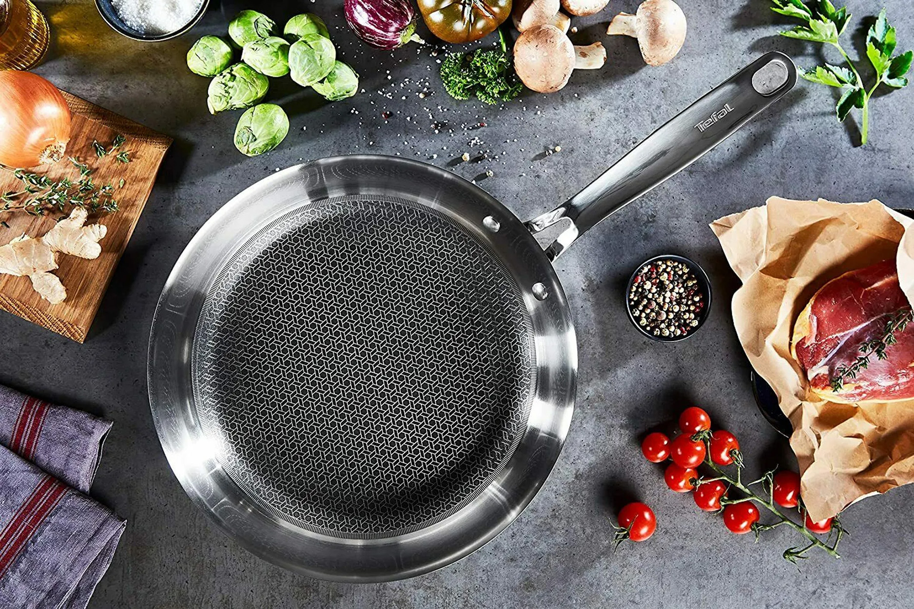 Edelstahlpfanne mit Zutaten. Enthält Gemüse, Gewürze und Fleisch auf dunkler grauer Oberfläche.