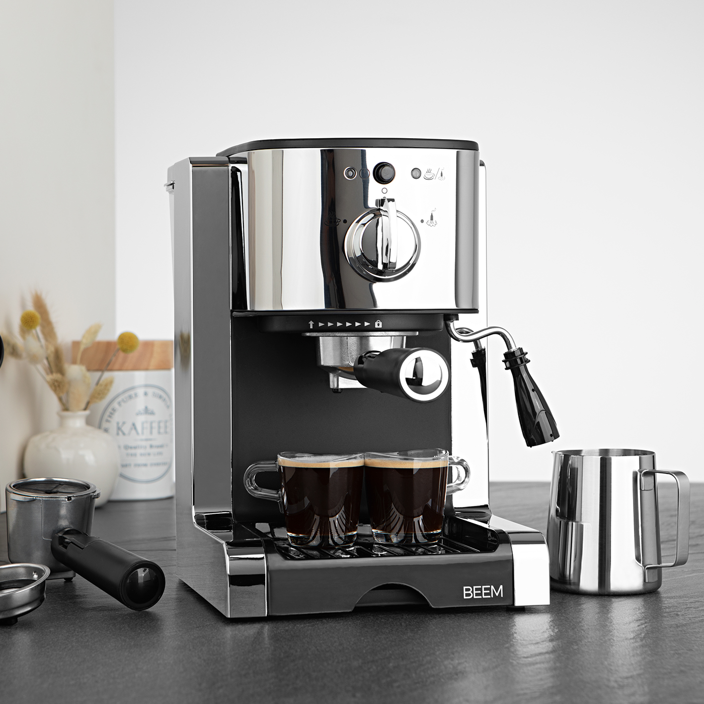 Chromowany i czarny ekspres do espresso z dwiema filiżankami. Na ciemnym blacie z akcesoriami.