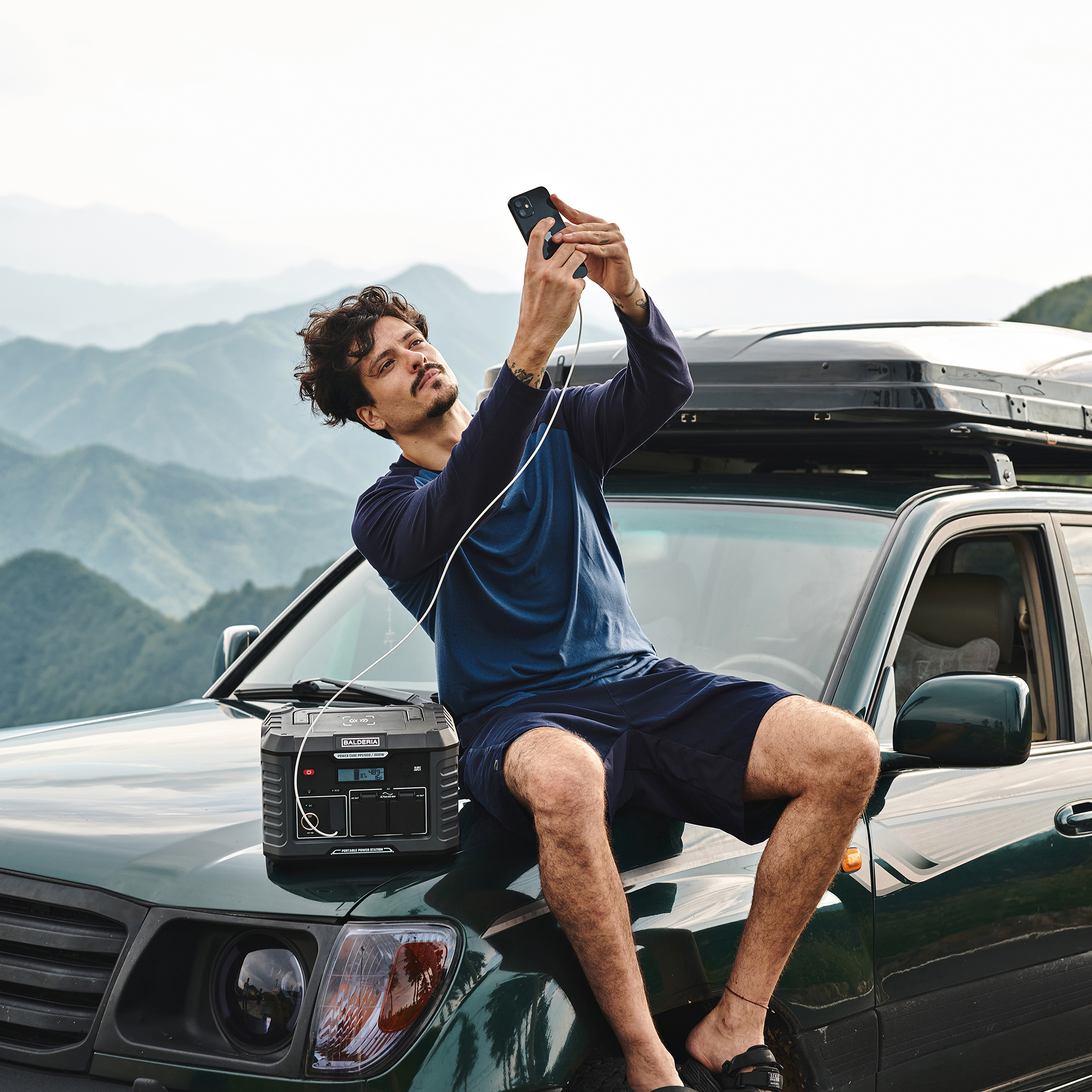 Mann macht Selfie beim Laden des Telefons mit einem Stromgenerator auf Auto.