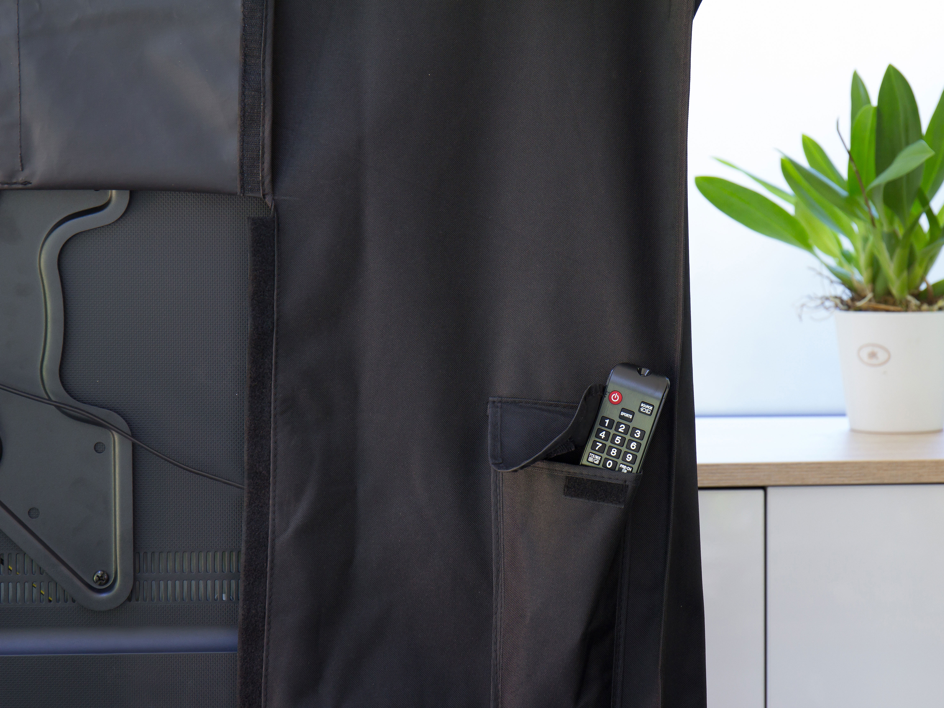 Schwarze TV-Abdeckung mit Fernbedienung in der Tasche. Eine Pflanze ist auf der rechten Seite.