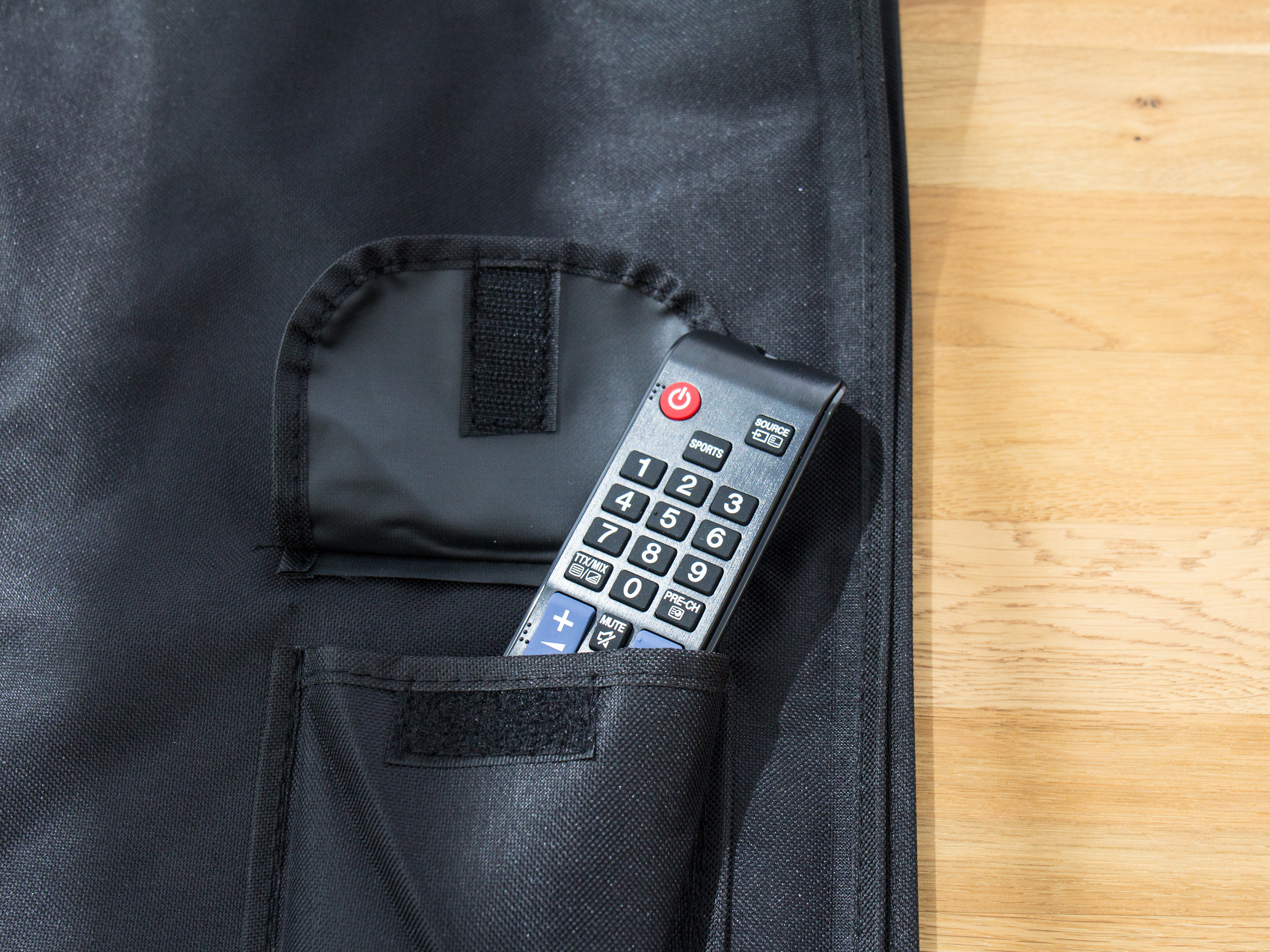 Schwarze Tasche mit Tasche, die eine TV-Fernbedienung enthält. Holzgrund.
