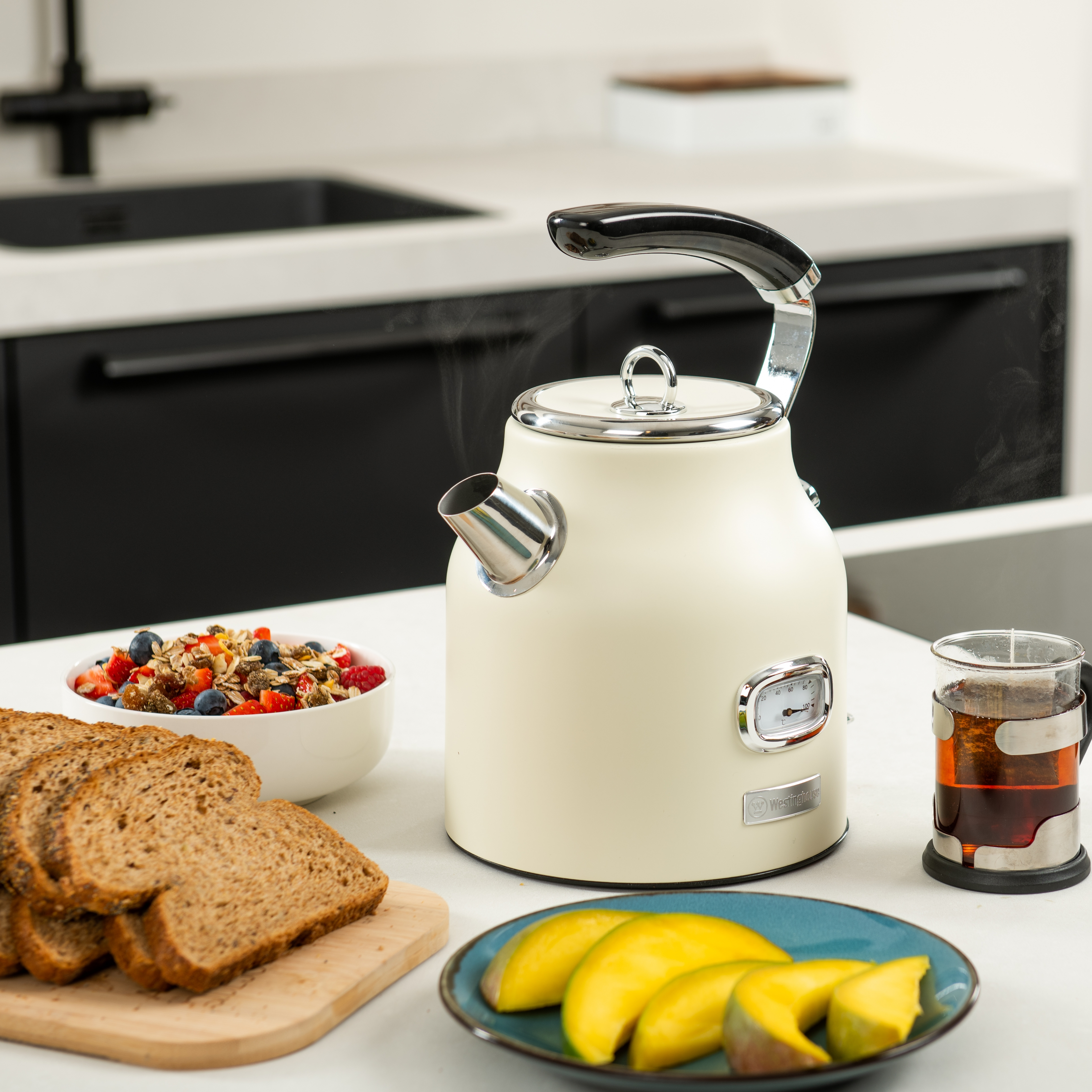 Ein weißer Wasserkocher mit Dampf, Frühstückszutaten wie Brot, Obst und eine Tasse Tee.