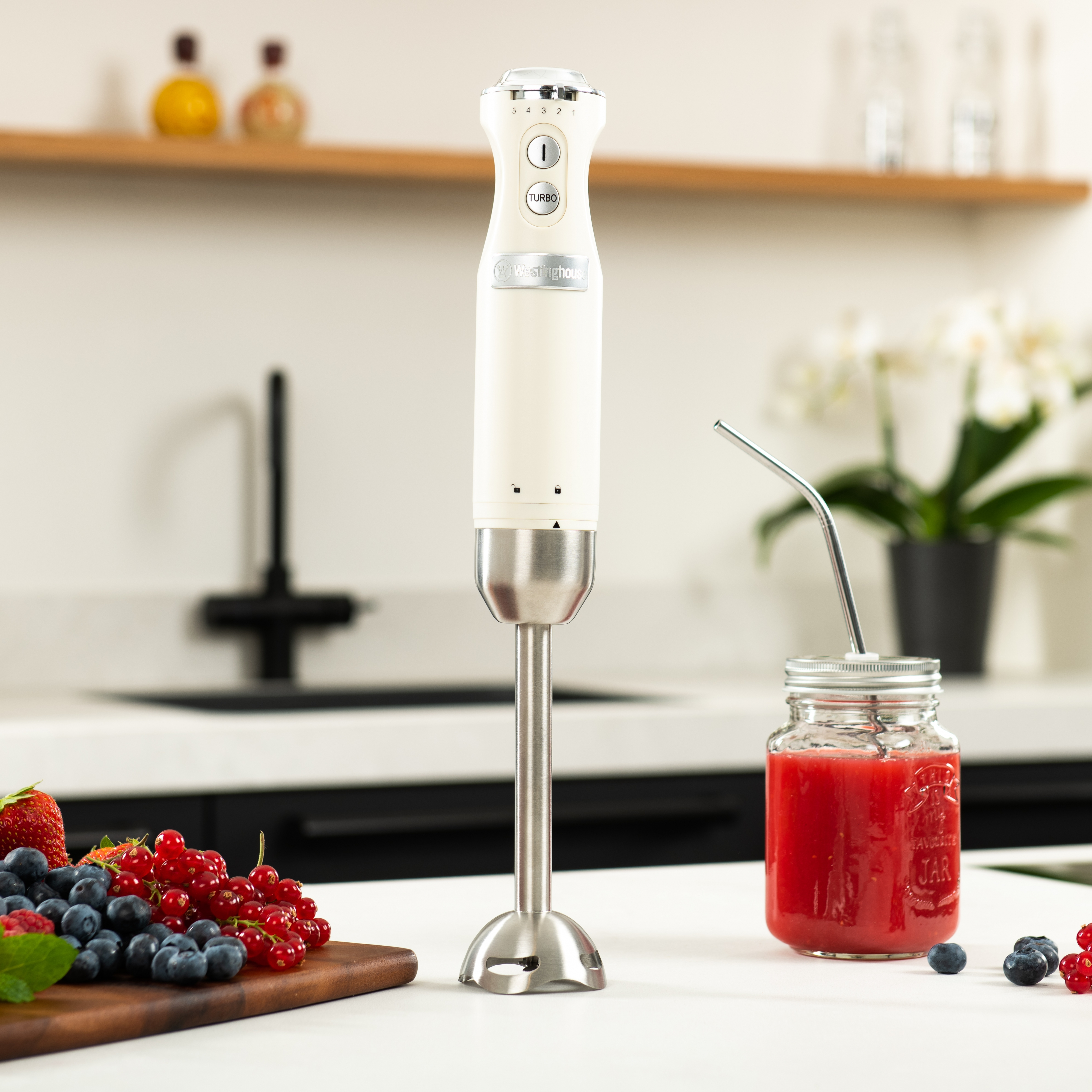 Stabmixer mit einem Glasbehälter mit roter Flüssigkeit, einem Holzbrett mit Beeren und einem Metallstrohhalm.