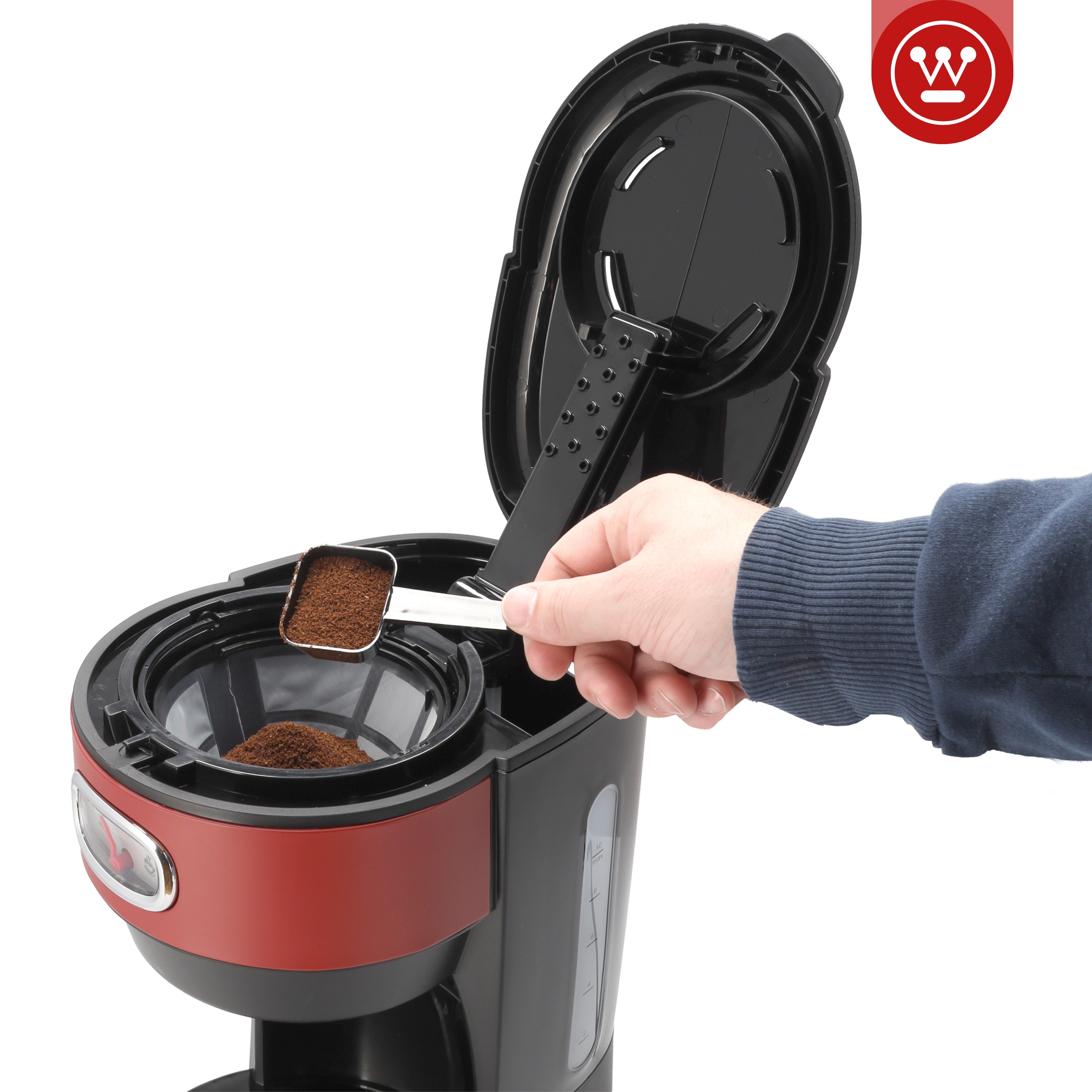 Eine Person fügt mit einem Löffel Kaffeepulver in den Filter einer Kaffeemaschine ein.