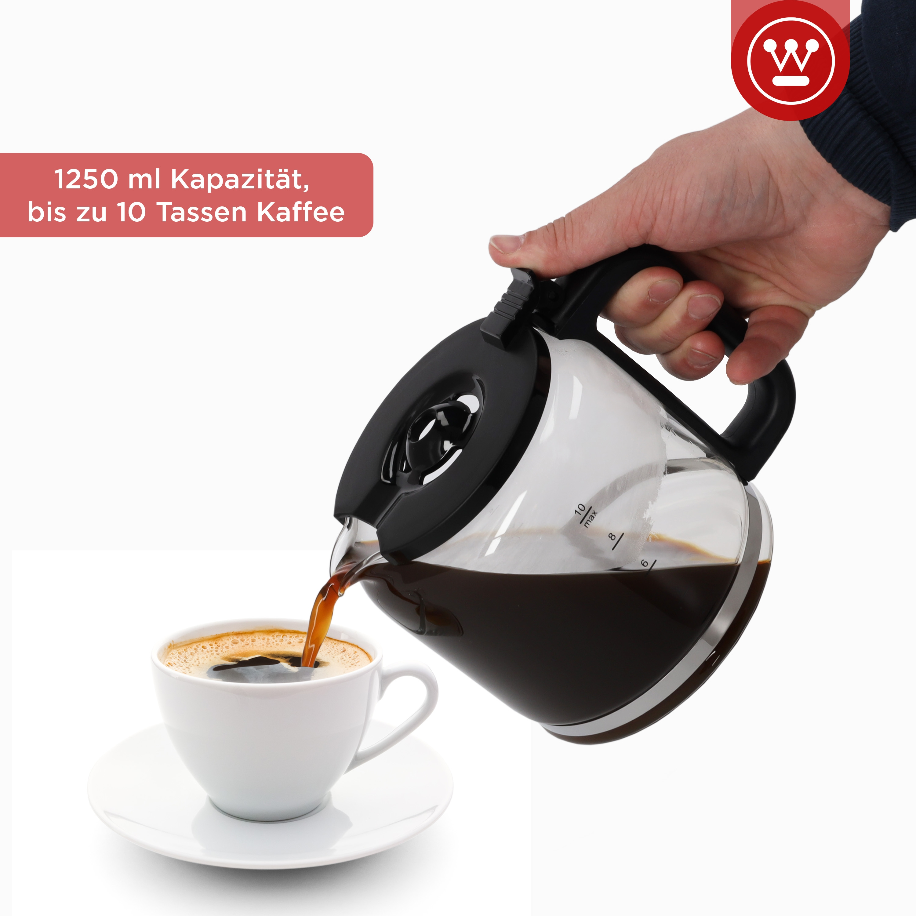 Eine Hand gießt Kaffee aus einer Glaskaraffe in eine weiße Tasse auf einer Untertasse.