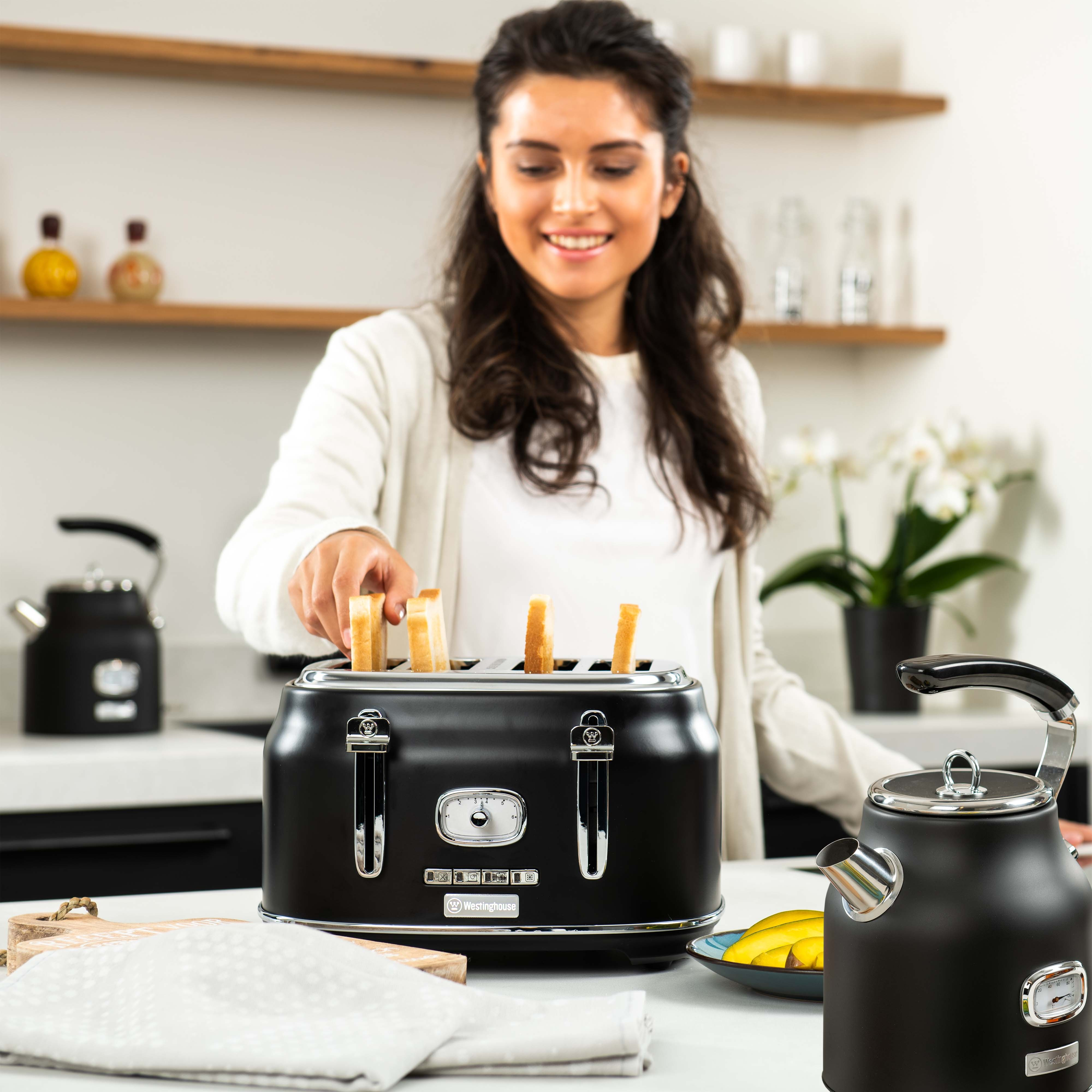 Frau benutzt einen schwarzen Toaster in einer Küche mit einem Wasserkocher und Bananen.