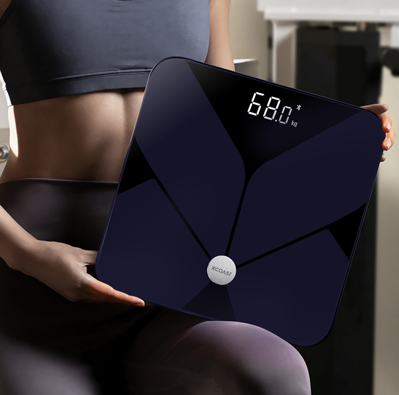 Eine Person hält eine dunkelblaue Smartwaage mit 68,0 kg auf dem Display.