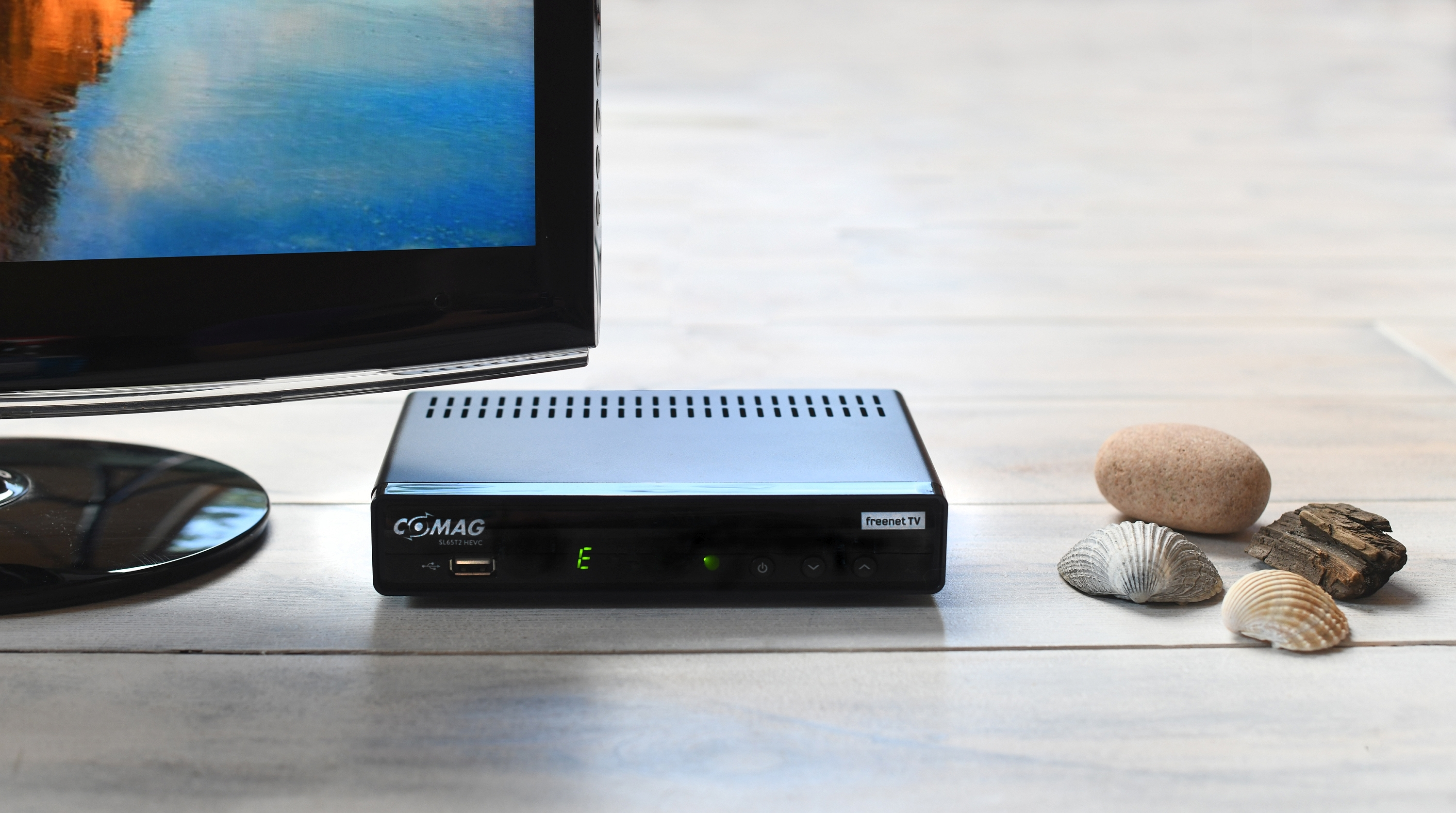 Schwarzer digitaler Empfänger mit Fernseher im Hintergrund und Steinen.