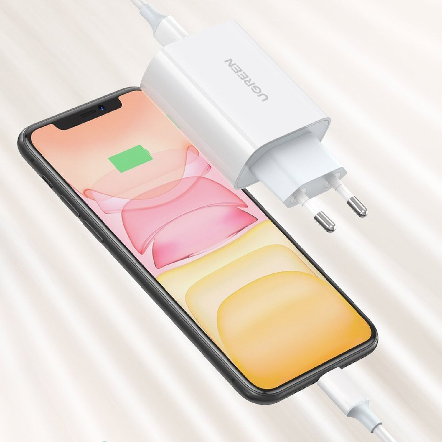 Weißes UGREEN-Ladegerät, das an ein Telefon angeschlossen ist und lädt, mit einem grünen Akkusymbol auf dem Bildschirm.