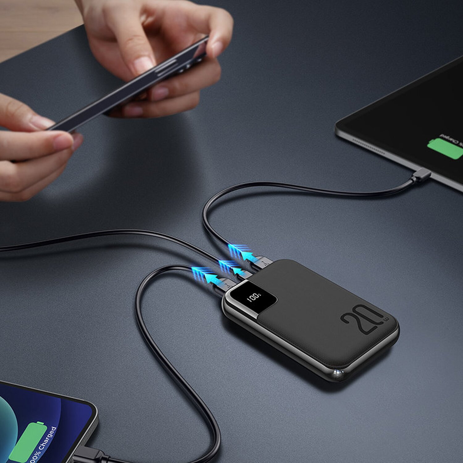 Schwarze Powerbank lädt zwei Telefone und ein Tablet. Hände des Nutzers sichtbar.