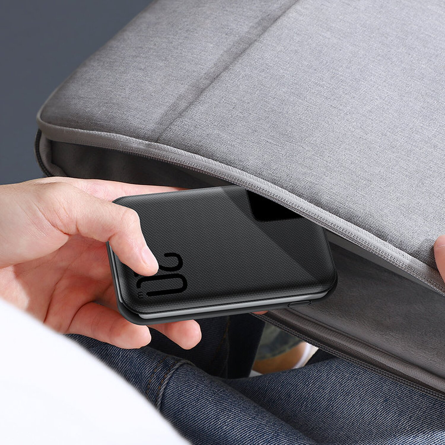 Hand hält ein schwarzes Telefon in einer grauen Laptoptasche.