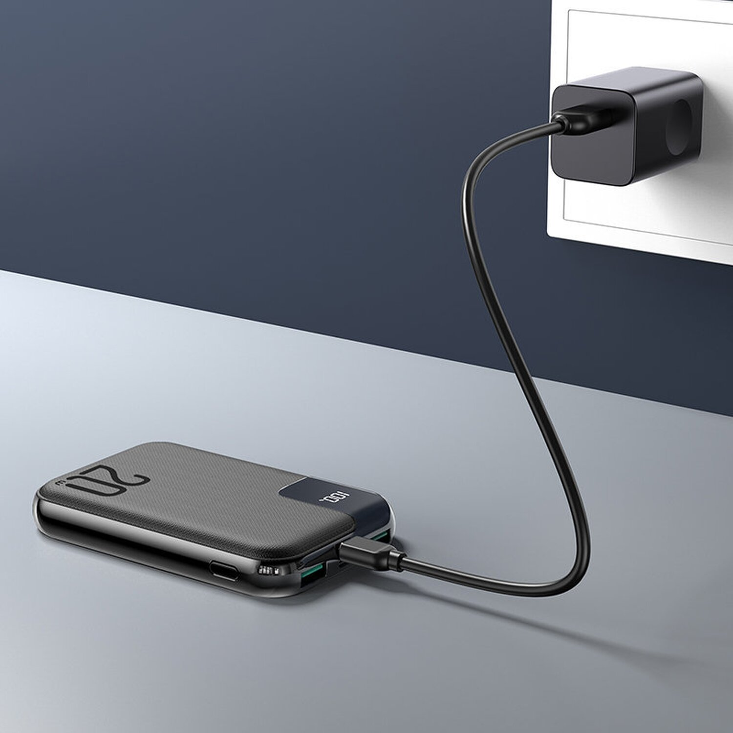 Eine schwarze Powerbank ist über ein schwarzes Kabel mit einer Steckdose verbunden.