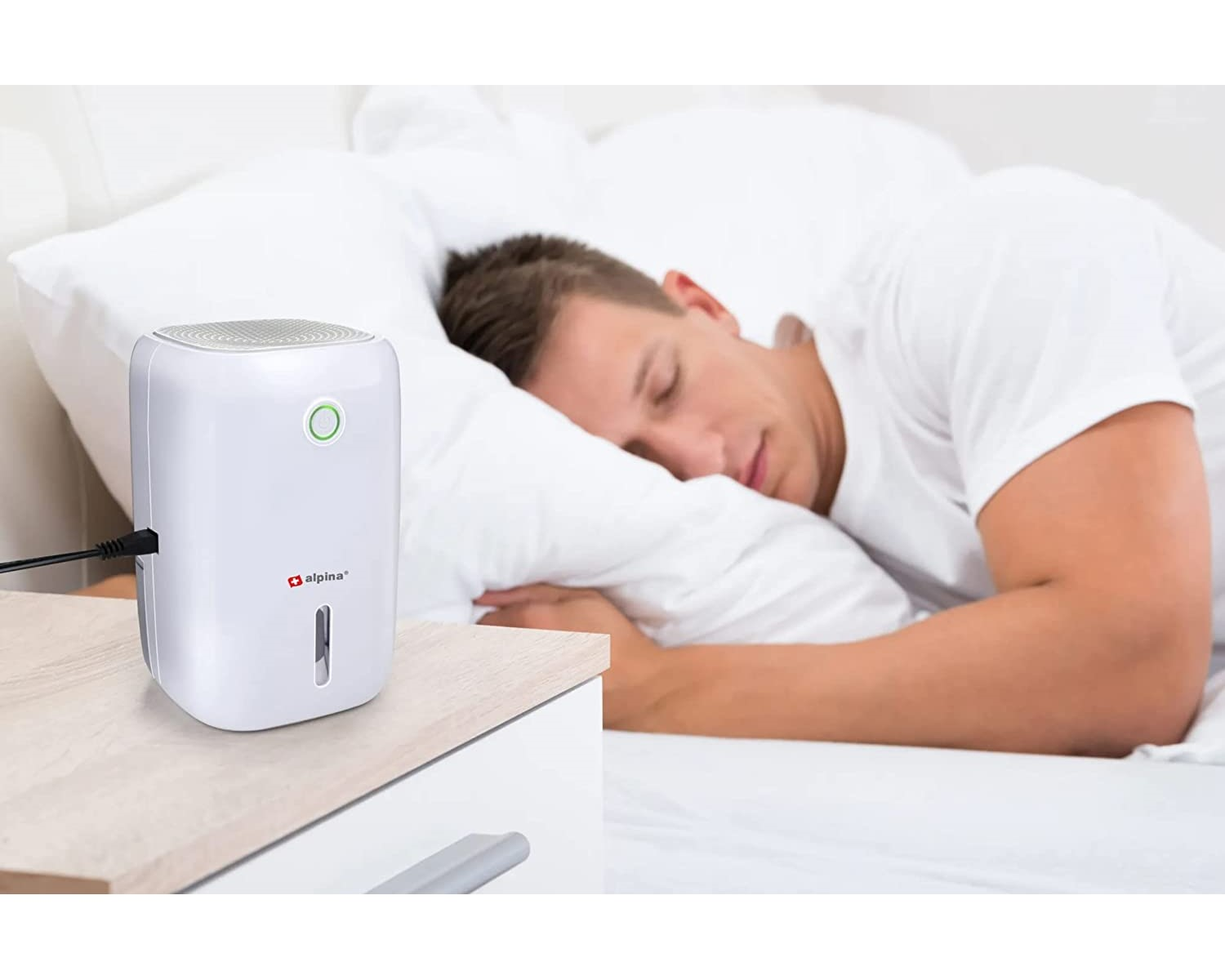 Mann schläft im Bett mit weißem Luftentfeuchter auf dem Nachttisch. Weiße Bettwäsche.