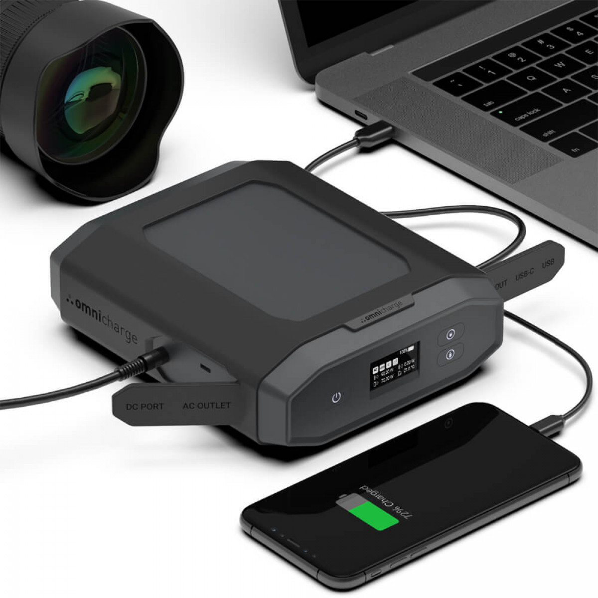 Power bank nero, laptop, telefono in carica. Obiettivo della fotocamera sullo sfondo.