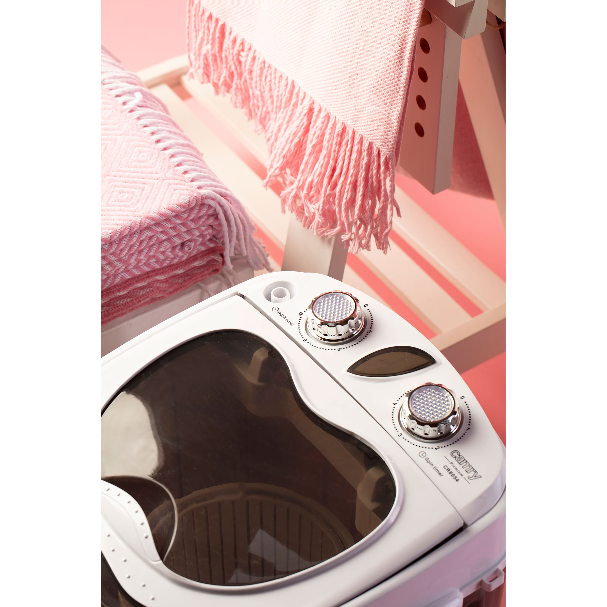 Biała pralka z dwoma różowymi kocami w tle.