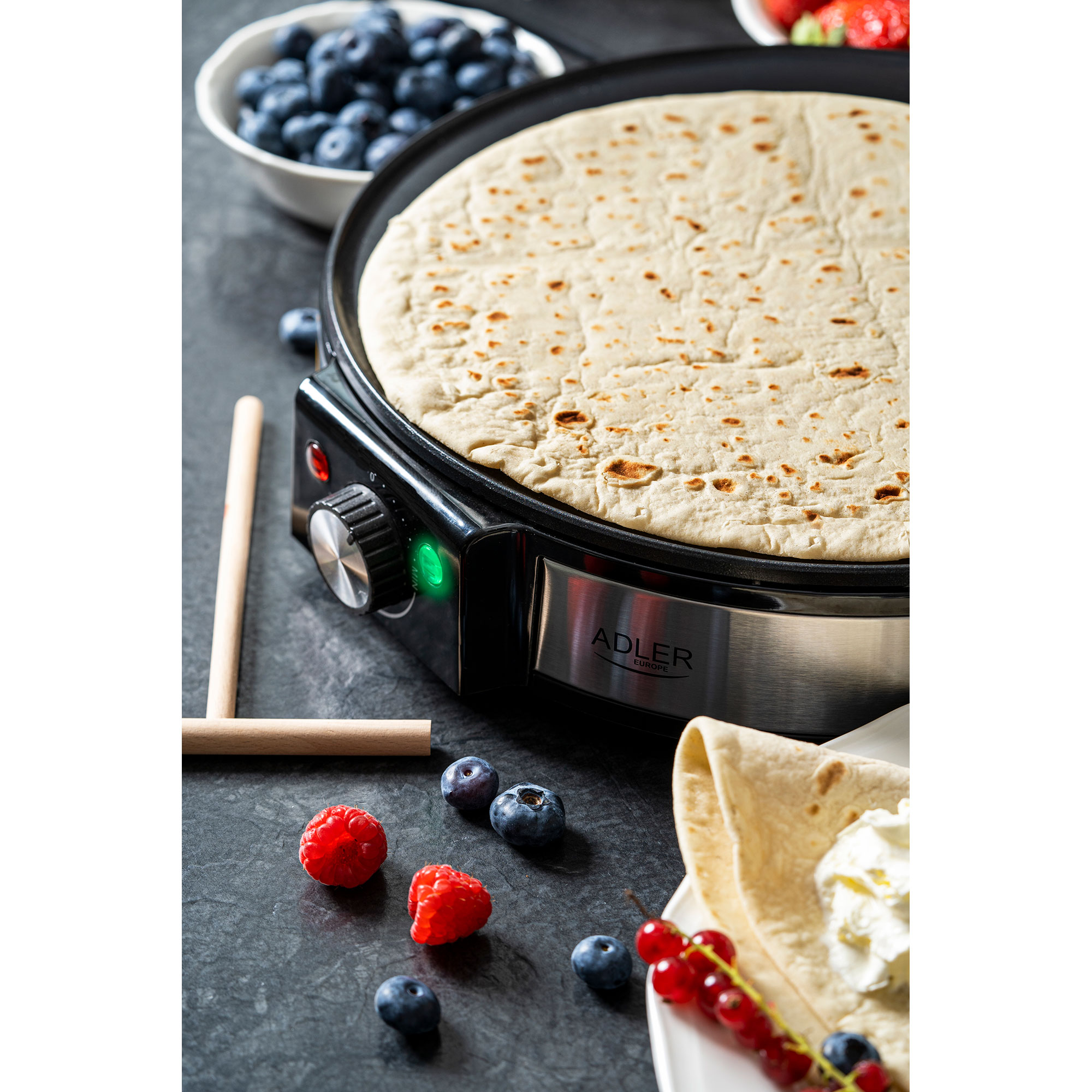 Naleśnik na czarnej płycie grzewczej z borówkami, malinami i porzeczkami.