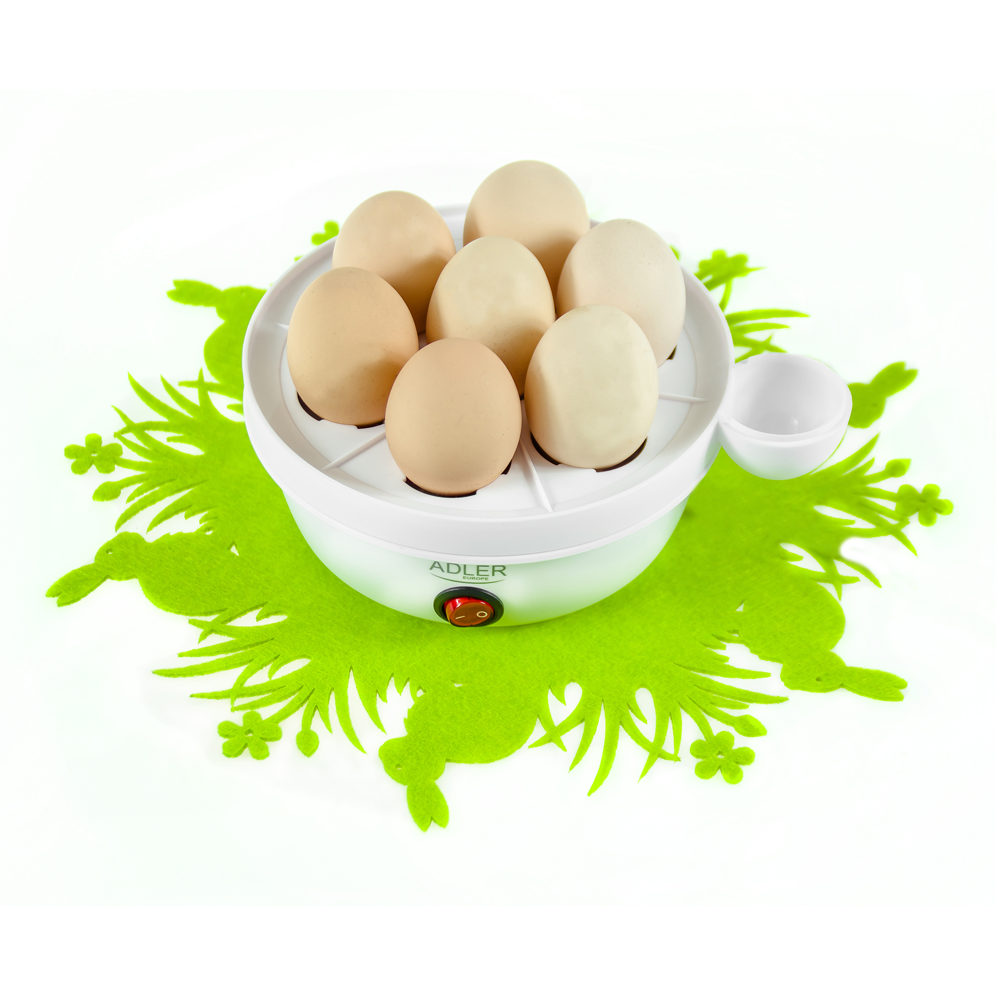 Olla para huevos blanca con huevos sobre una alfombra verde. El aparato tiene un botón rojo.