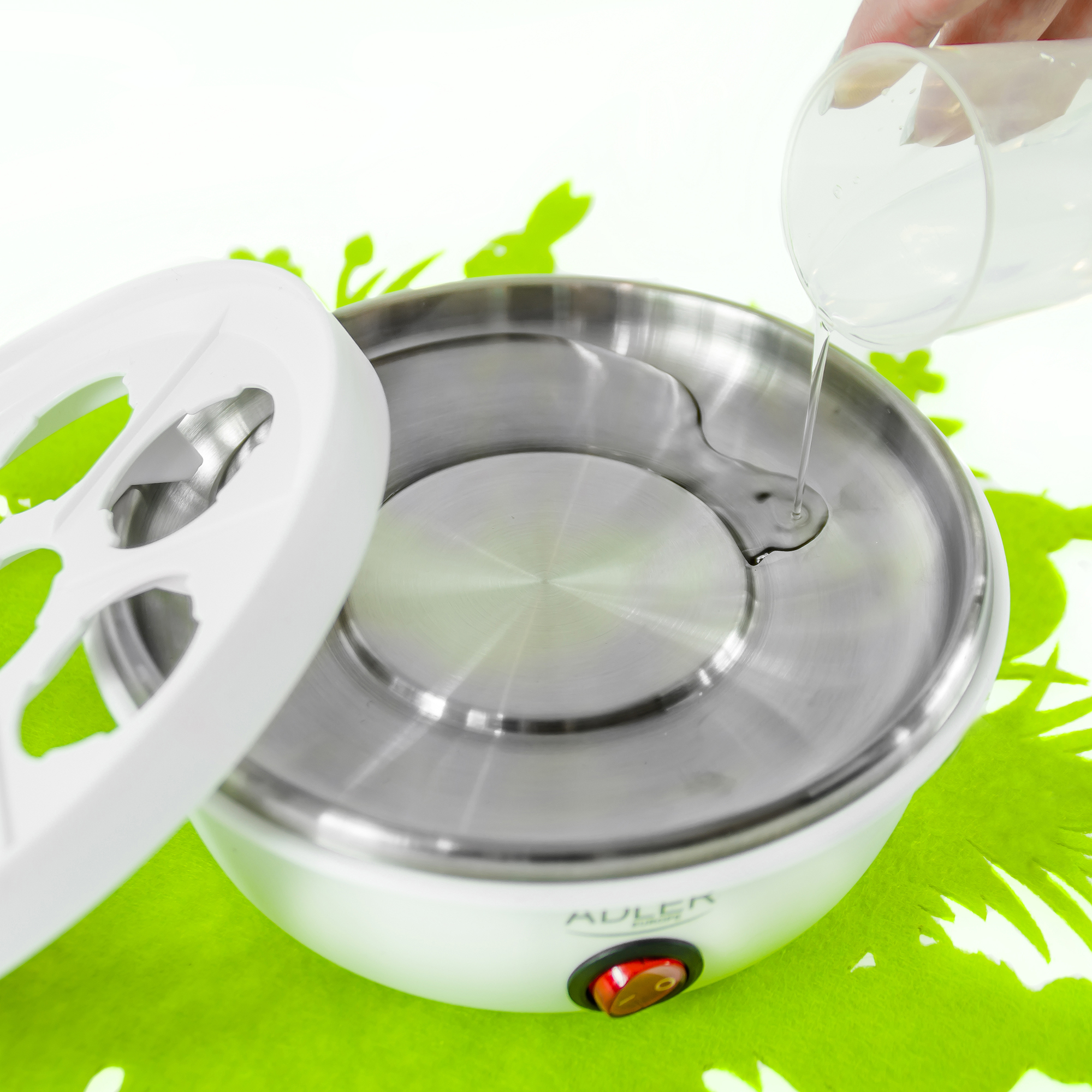 Huevera con agua vertiéndose desde una taza medidora transparente. Fondo verde.