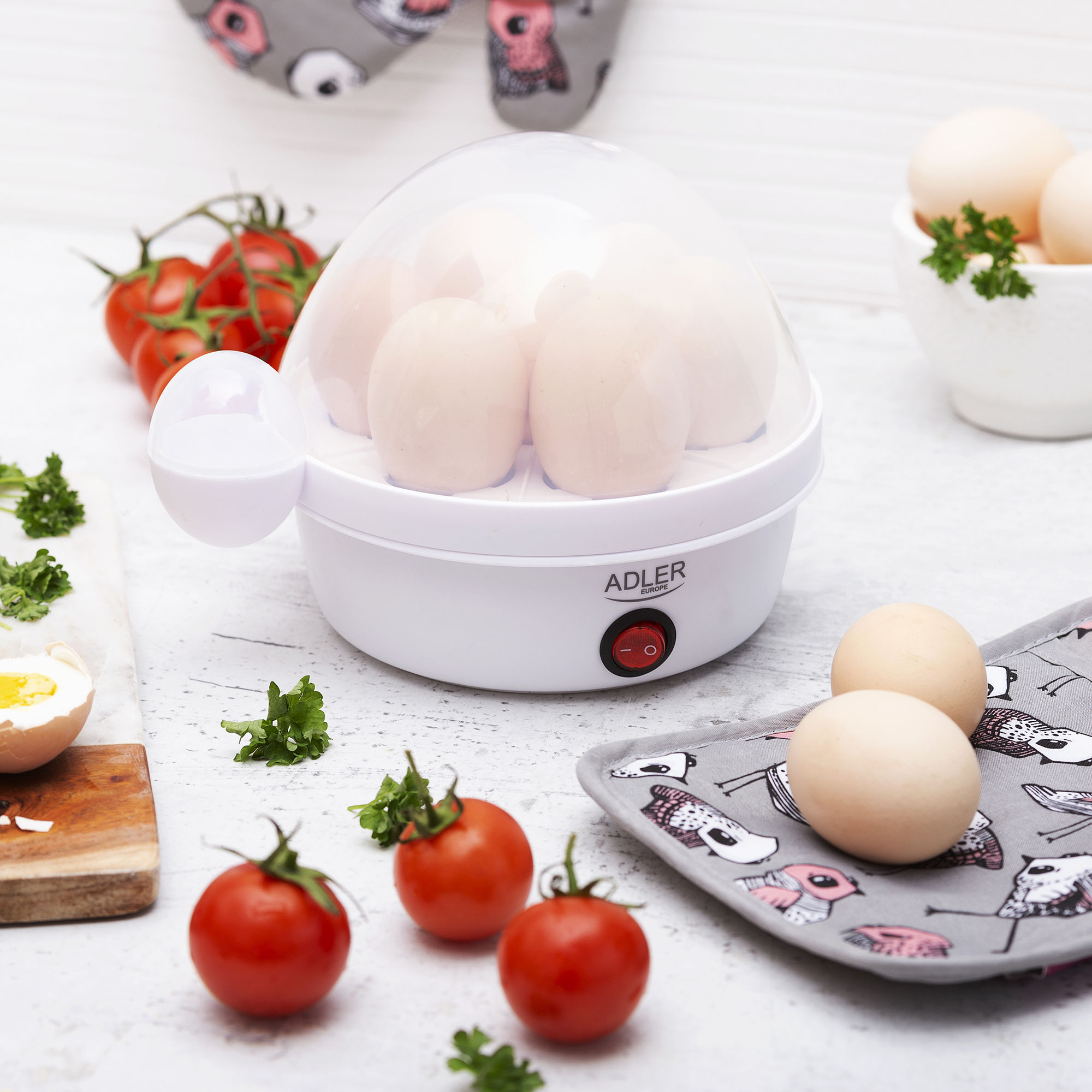 Hervidor de huevos blanco con huevos, tomates, perejil y huevo en tabla de madera.