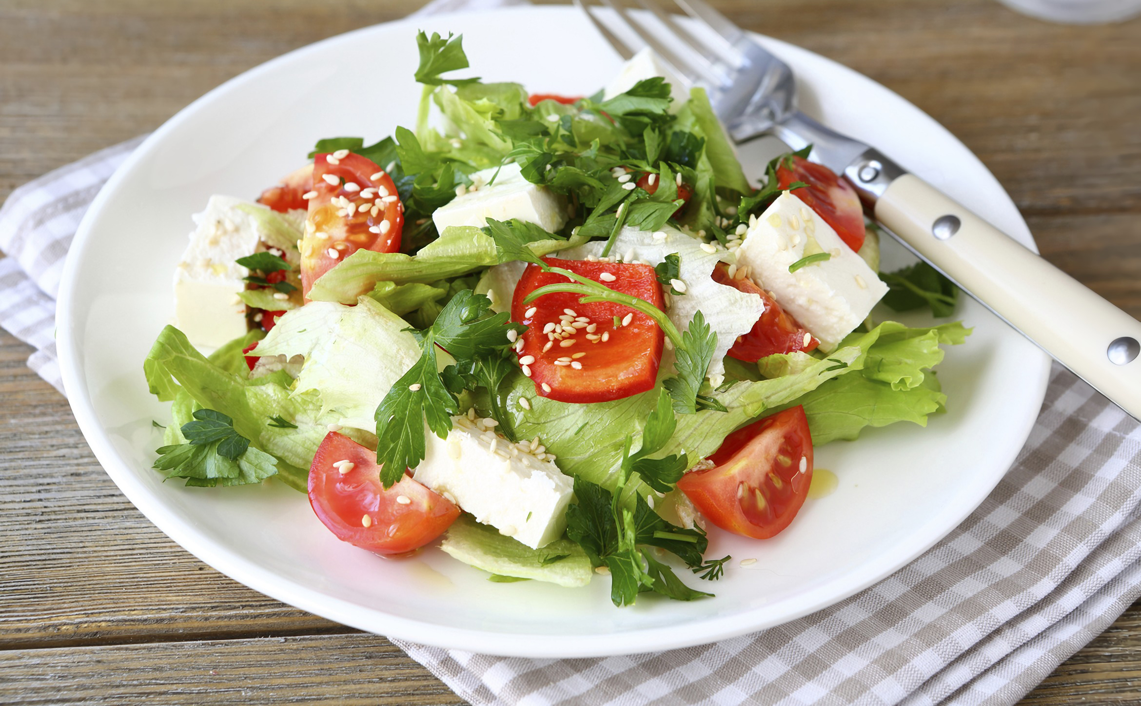 Ensalada en plato blanco con lechuga, tomates, feta y perejil, mesa de madera.