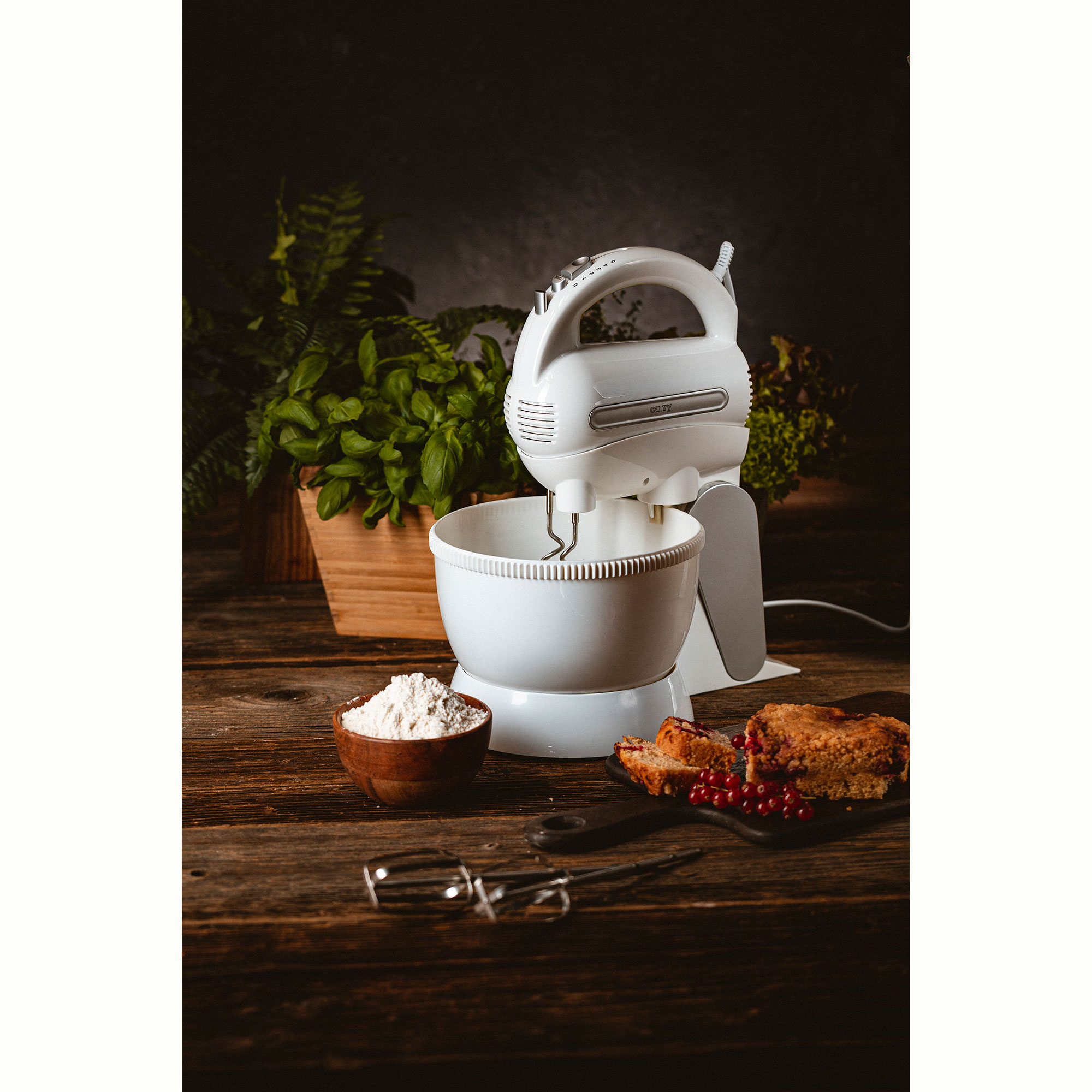 Biały mikser, miska z mąką, drewniana miska z mąką, kawałki ciasta, na drewnianym stole.