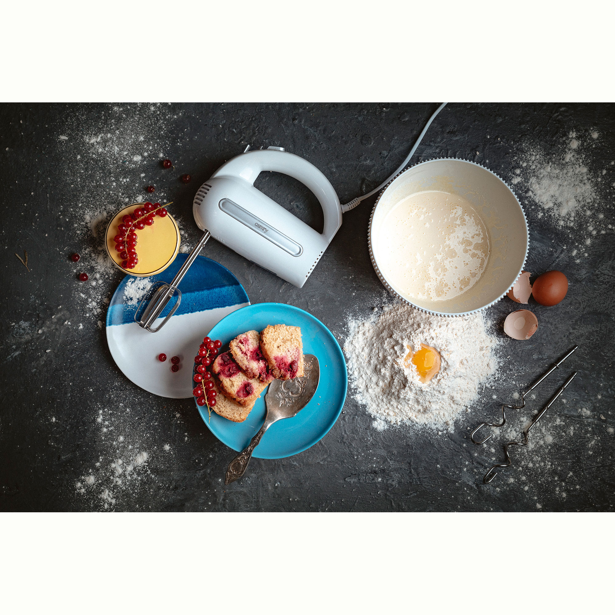 Scena pieczenia ze składnikami, mikserem i talerzami ciasta. Mąka jest rozsypana na powierzchni.