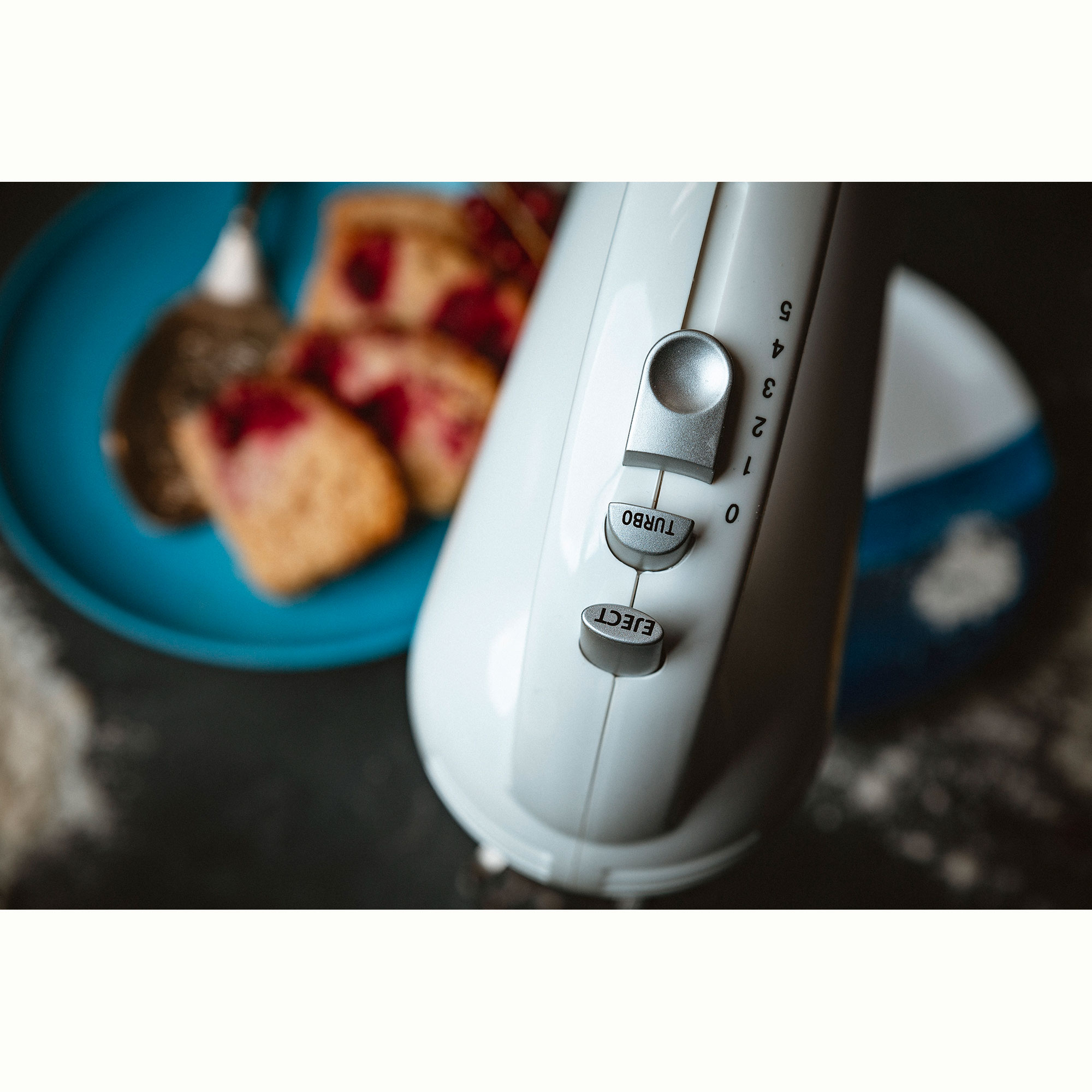 Zbliżenie białego miksera ręcznego z regulatorami prędkości i częściowo rozmytym ciastem.