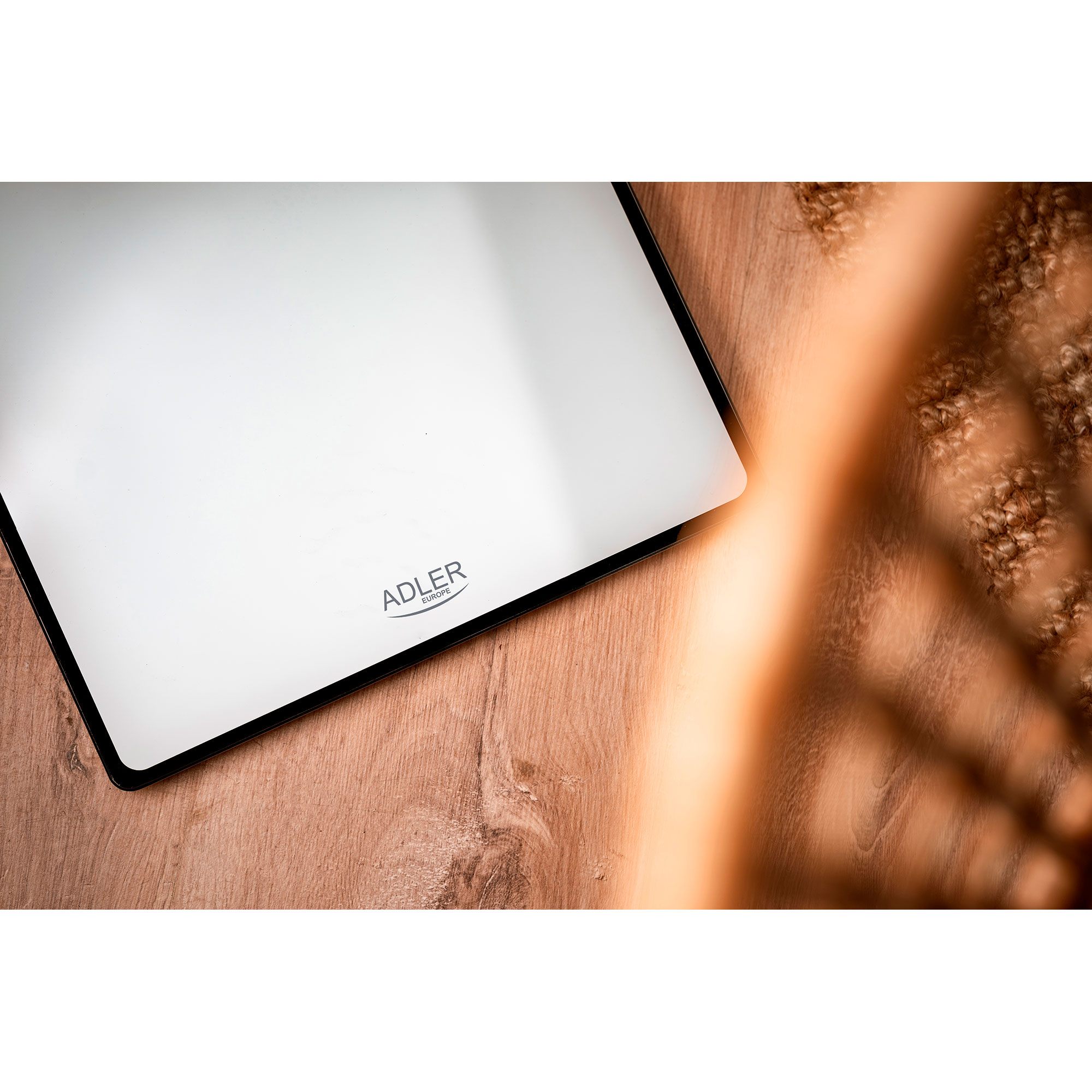 Biała waga cyfrowa z czarną obwódką, na drewnianej podłodze.