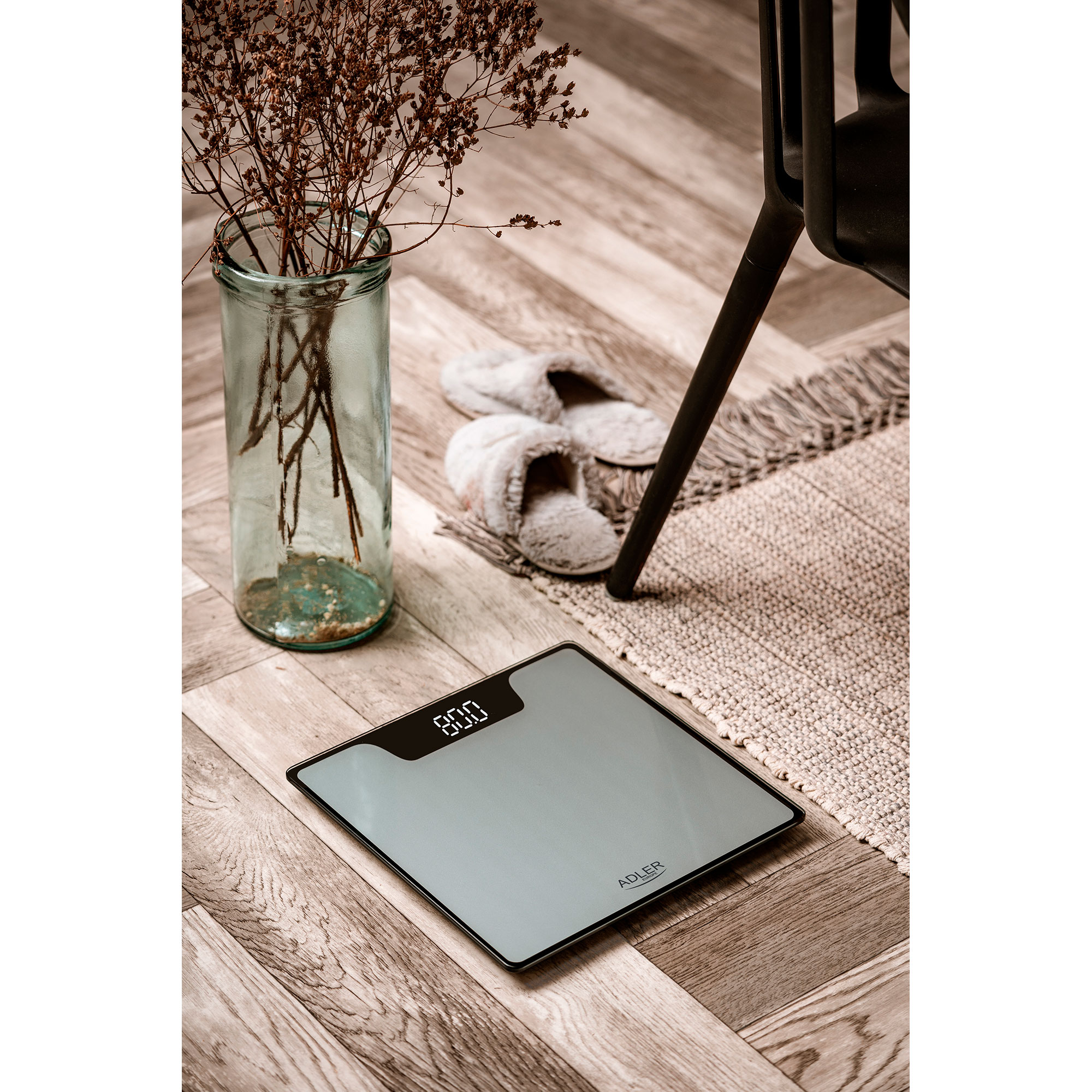 Waga cyfrowa z wagą 80.0, obok kapci, wazonu i drewnianej podłogi.