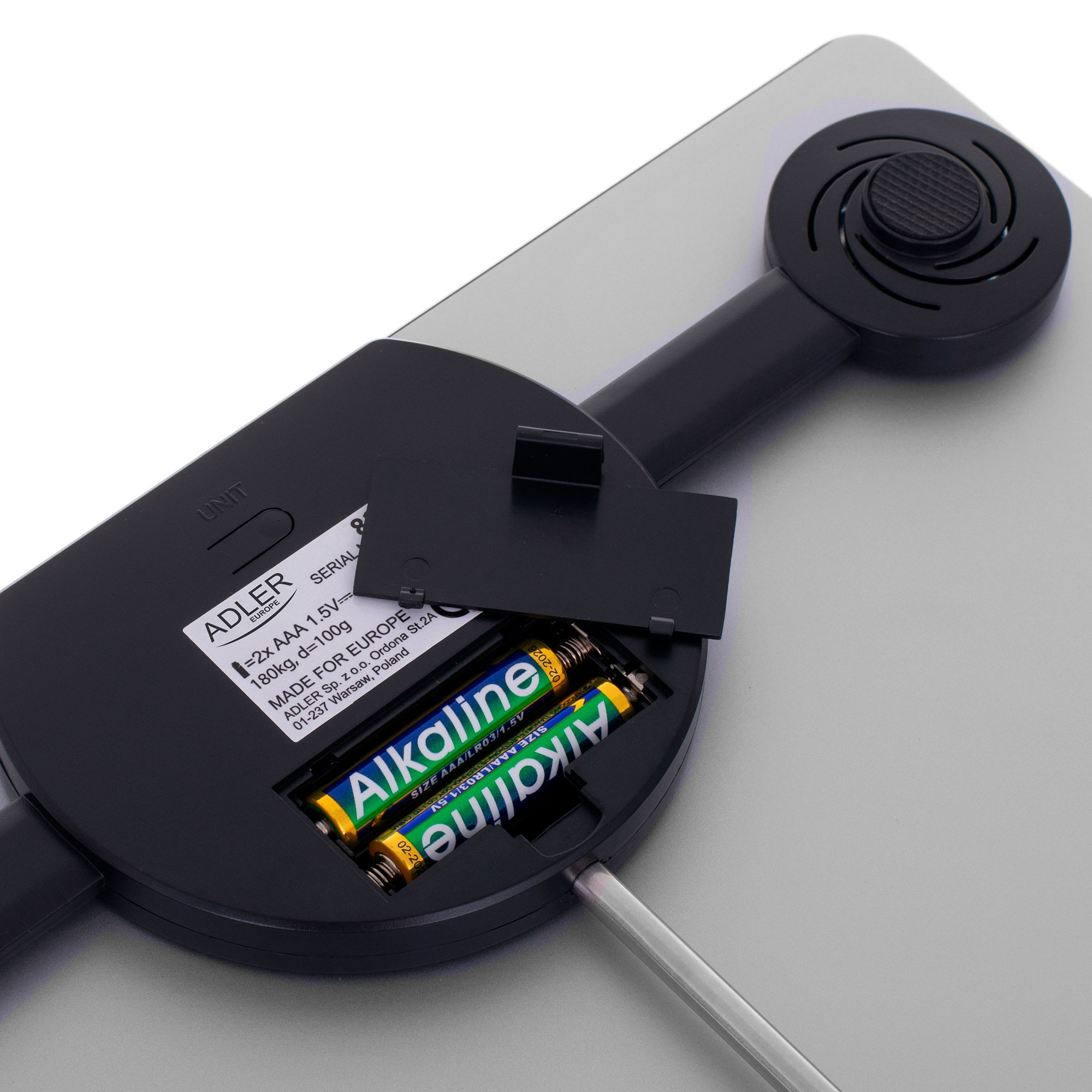 Widok z góry na wagę z otwartą komorą baterii, ujawniającą dwie baterie alkaliczne.