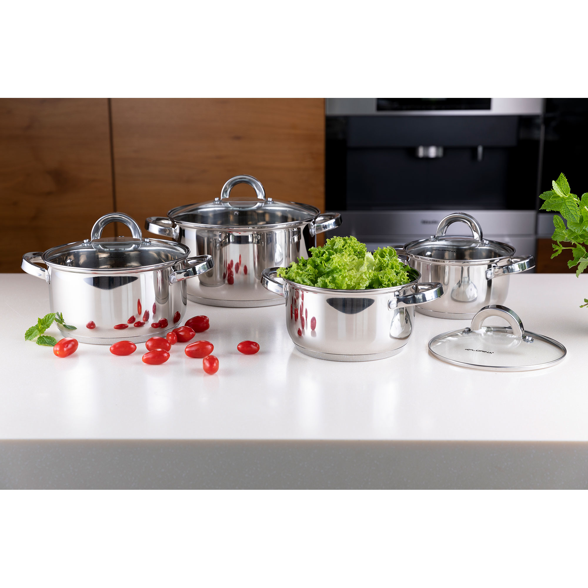 Ollas brillantes de acero inoxidable con tapas de vidrio, algunas con lechuga y tomates.