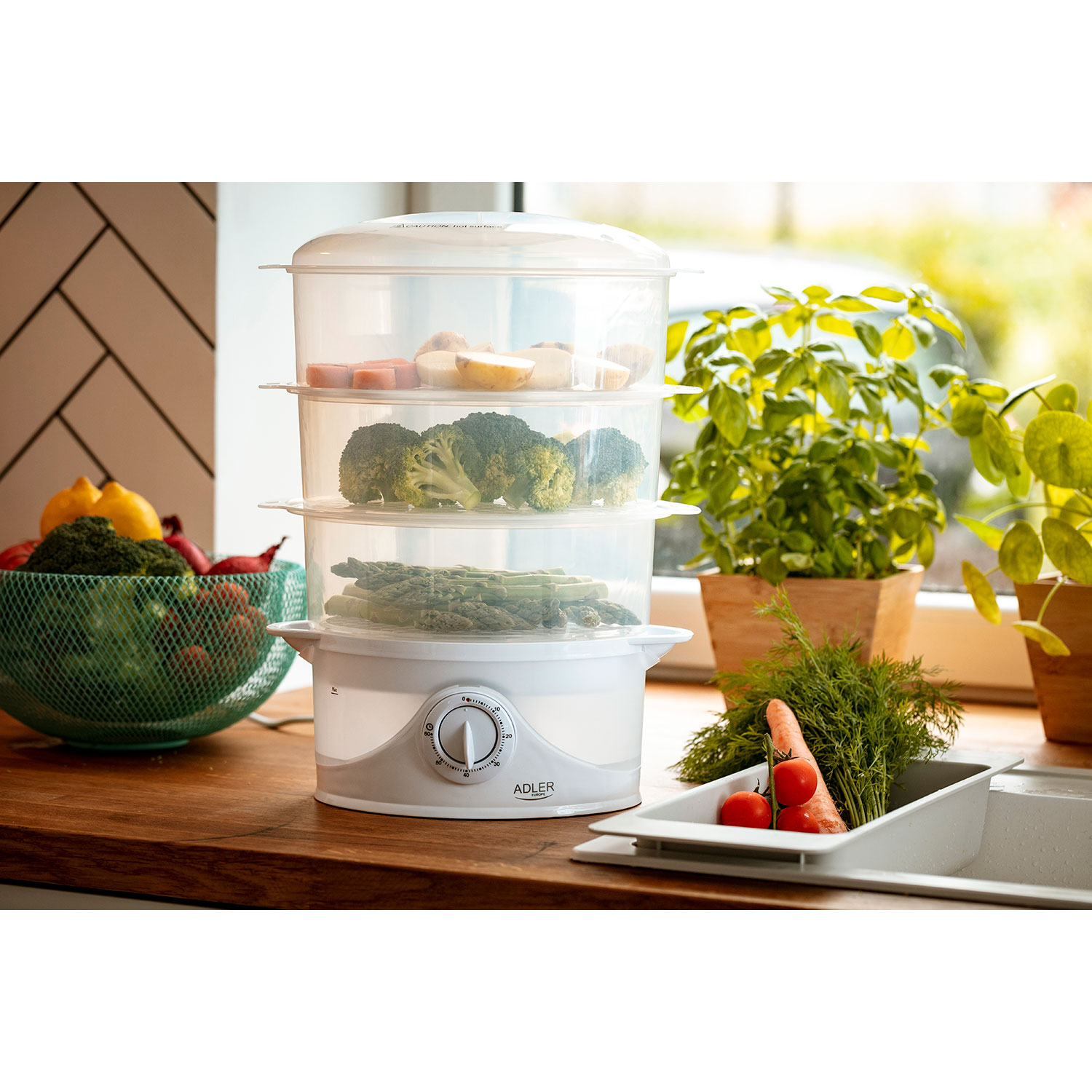 Vaporera con tres niveles, con verduras. Brócoli, espárragos y zanahorias. Sobre una encimera de madera, junto a una ventana.