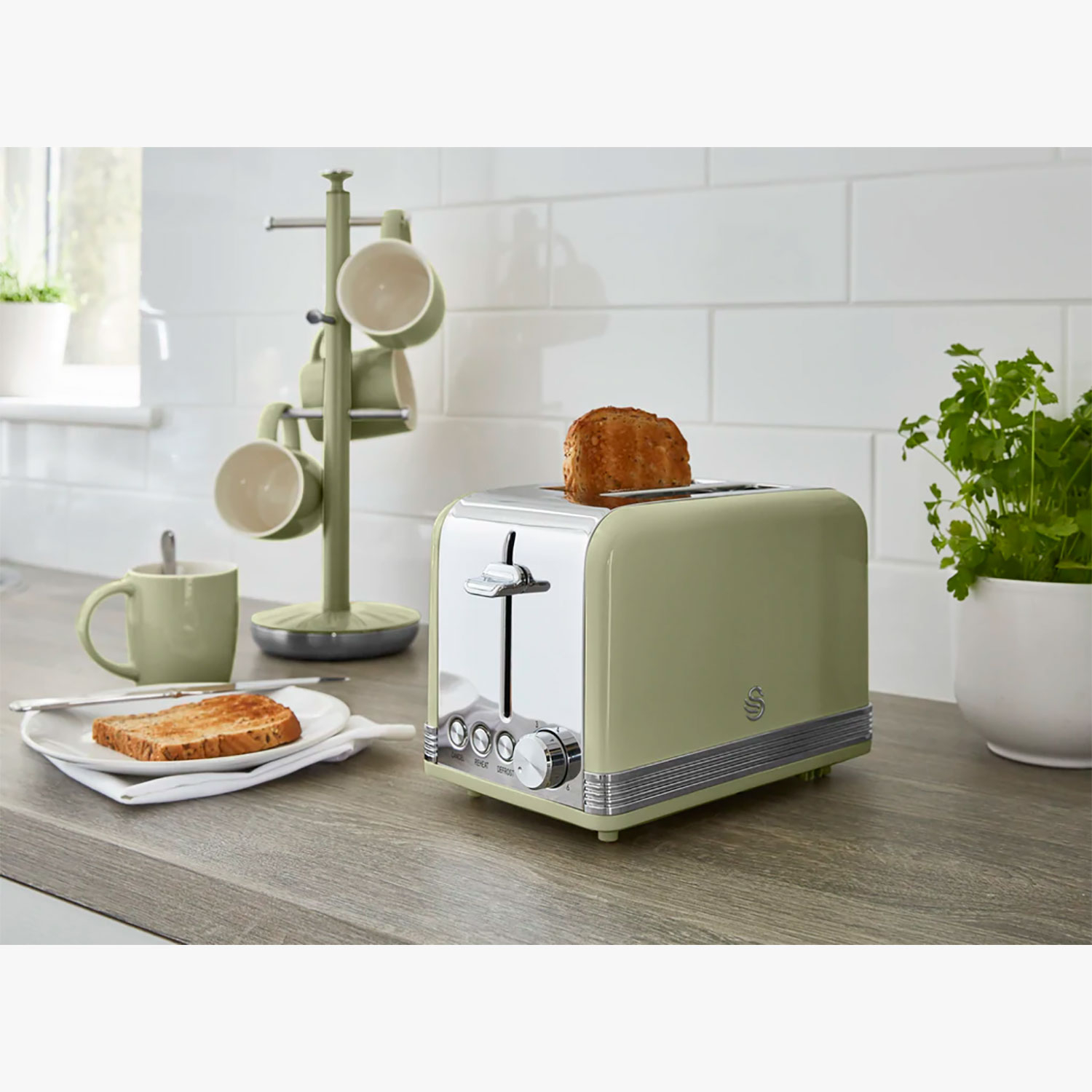 Grüner Toaster mit einer Toastscheibe. Eine Tasse und ein Becherhalter sind daneben.