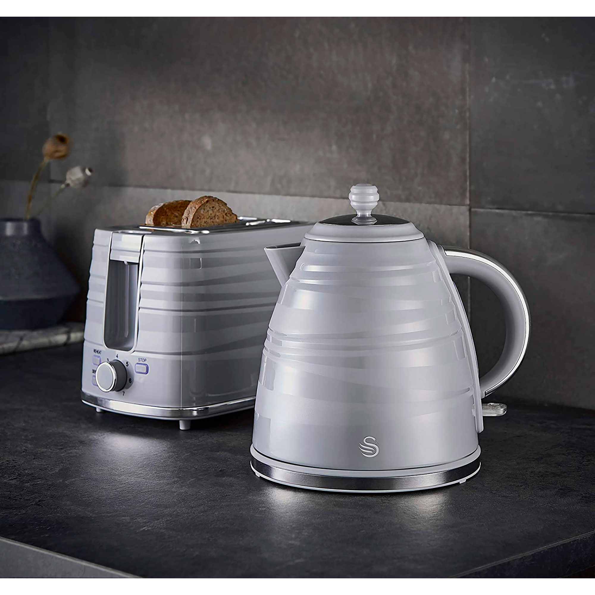 Grey toaster and kettle set on dark surface. Toaster with bread, kettle with swan logo.