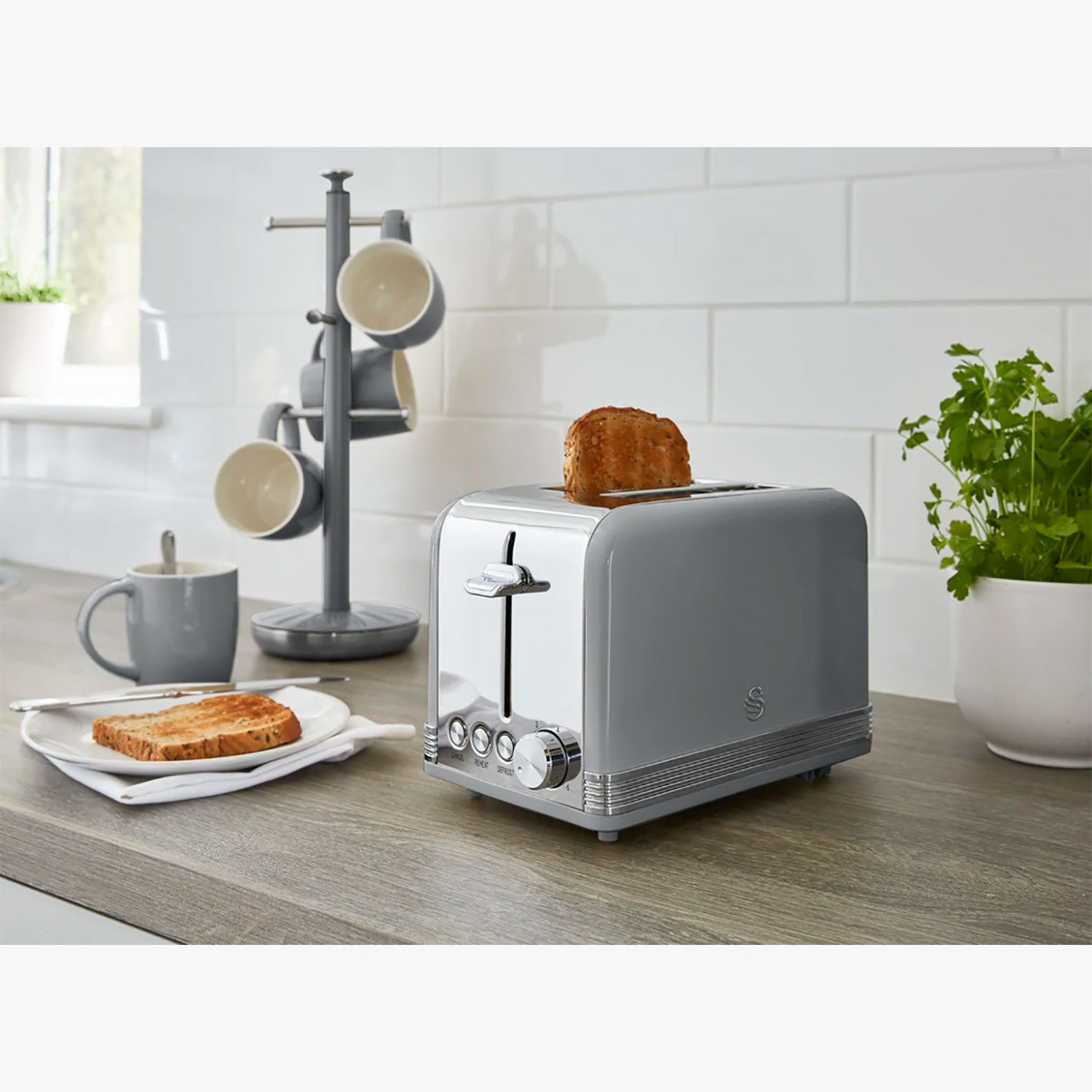 Un tostapane grigio con una fetta di pane tostato, una tazza e un portabicchieri.