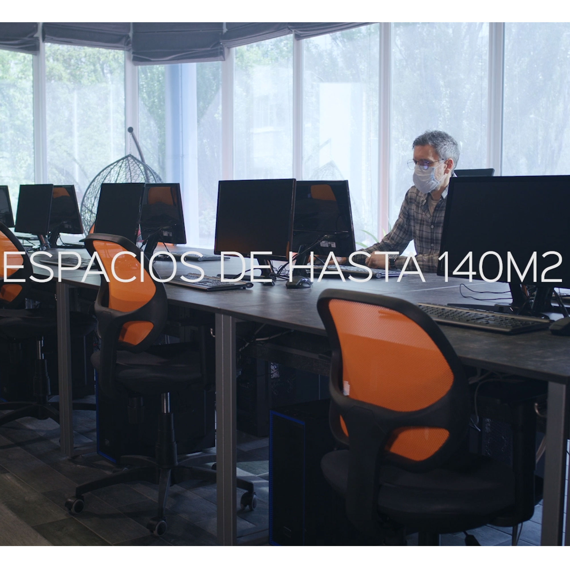 Büro mit Schreibtischen, Computern und einem Angestellten mit Maske, orangefarbene Stühle.