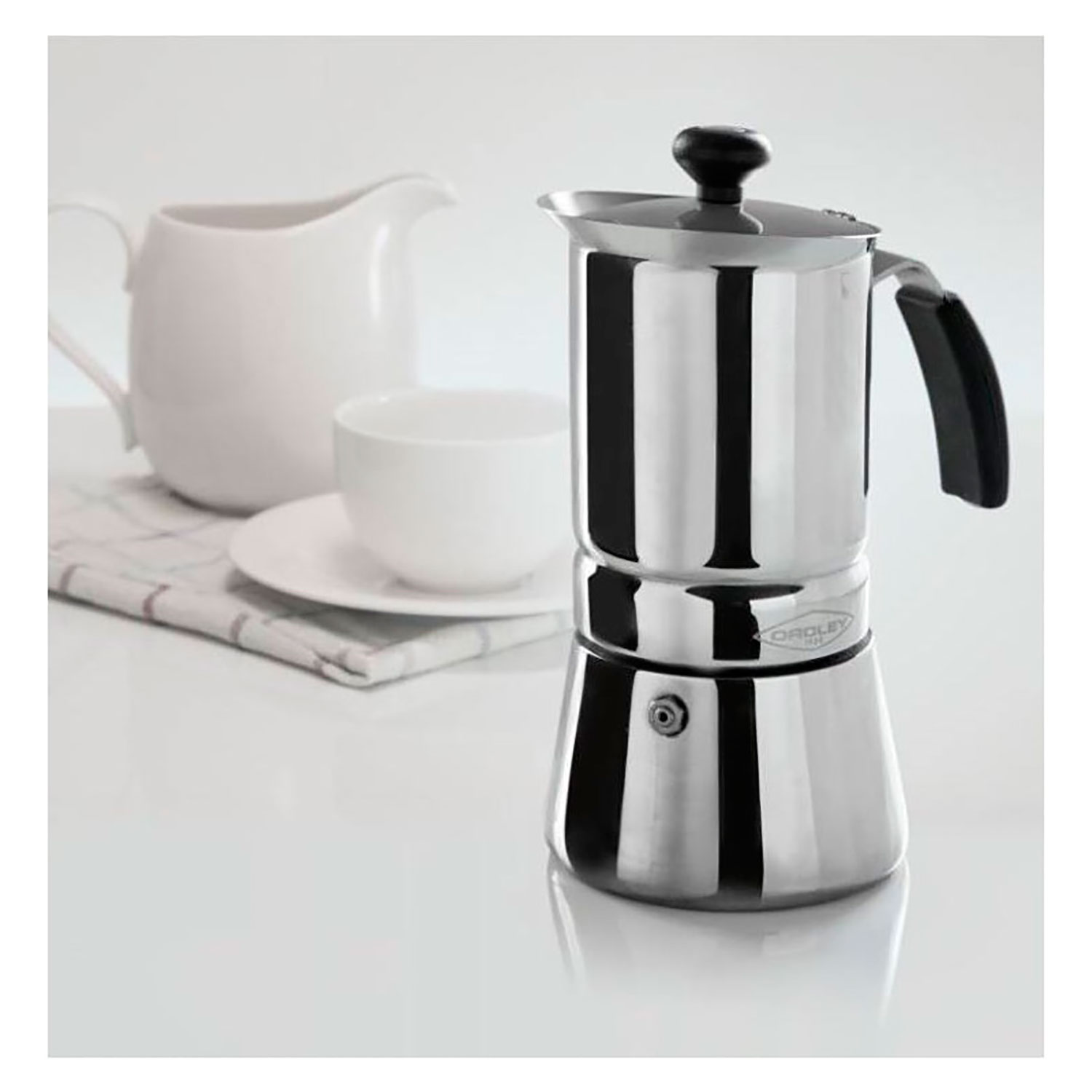 Una cafetera exprés de acero inoxidable, una crema blanca y una taza.