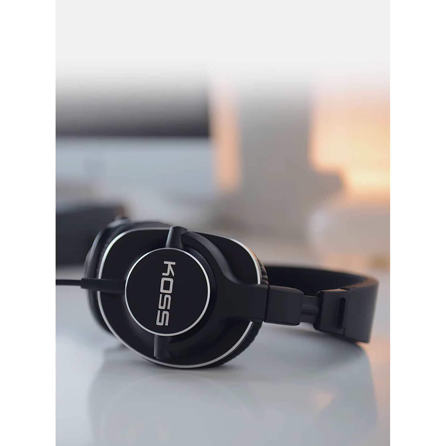 Czarne słuchawki z napisem KOSS na nauszniku. Słuchawki leżą na białej powierzchni.