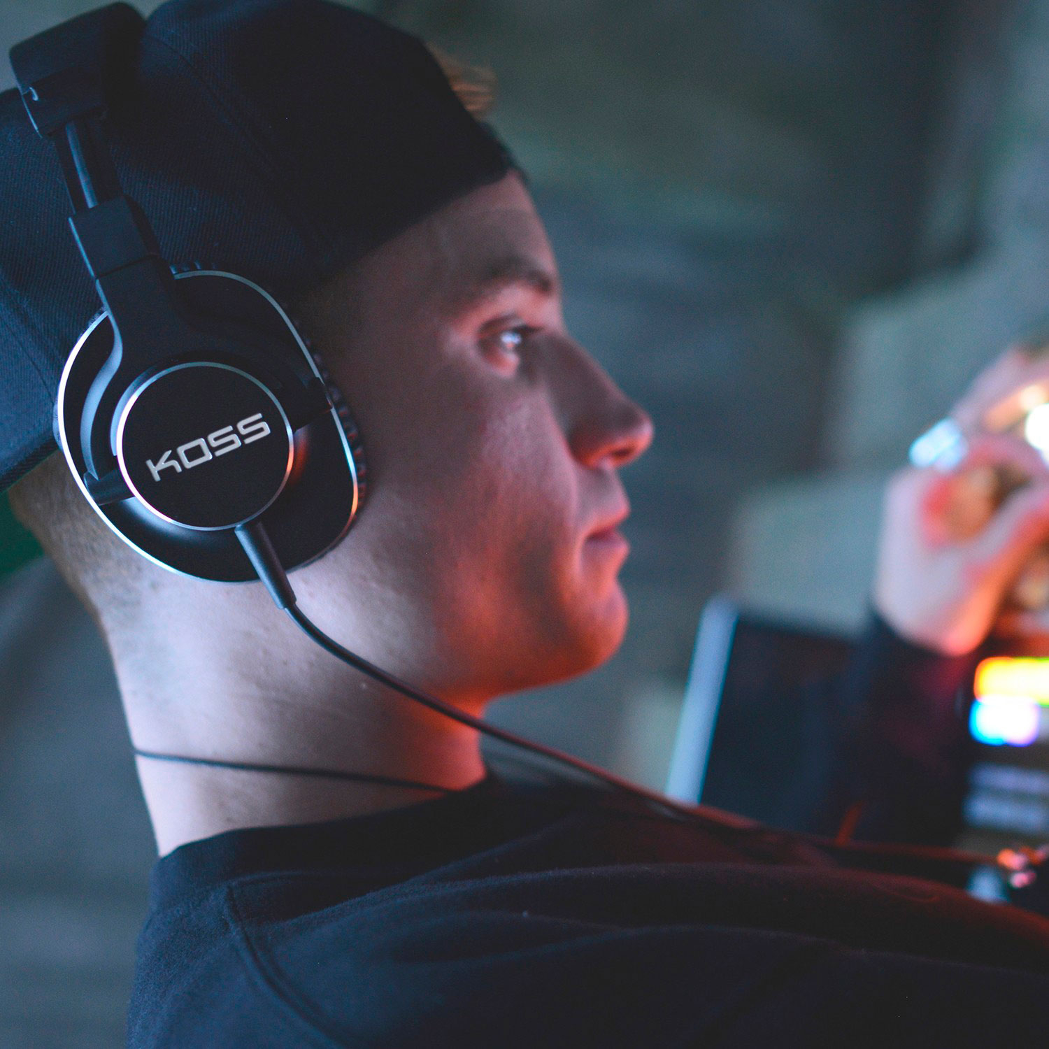 Mężczyzna w słuchawkach. Słuchawki mają napis KOSS. Tło jest rozmyte.