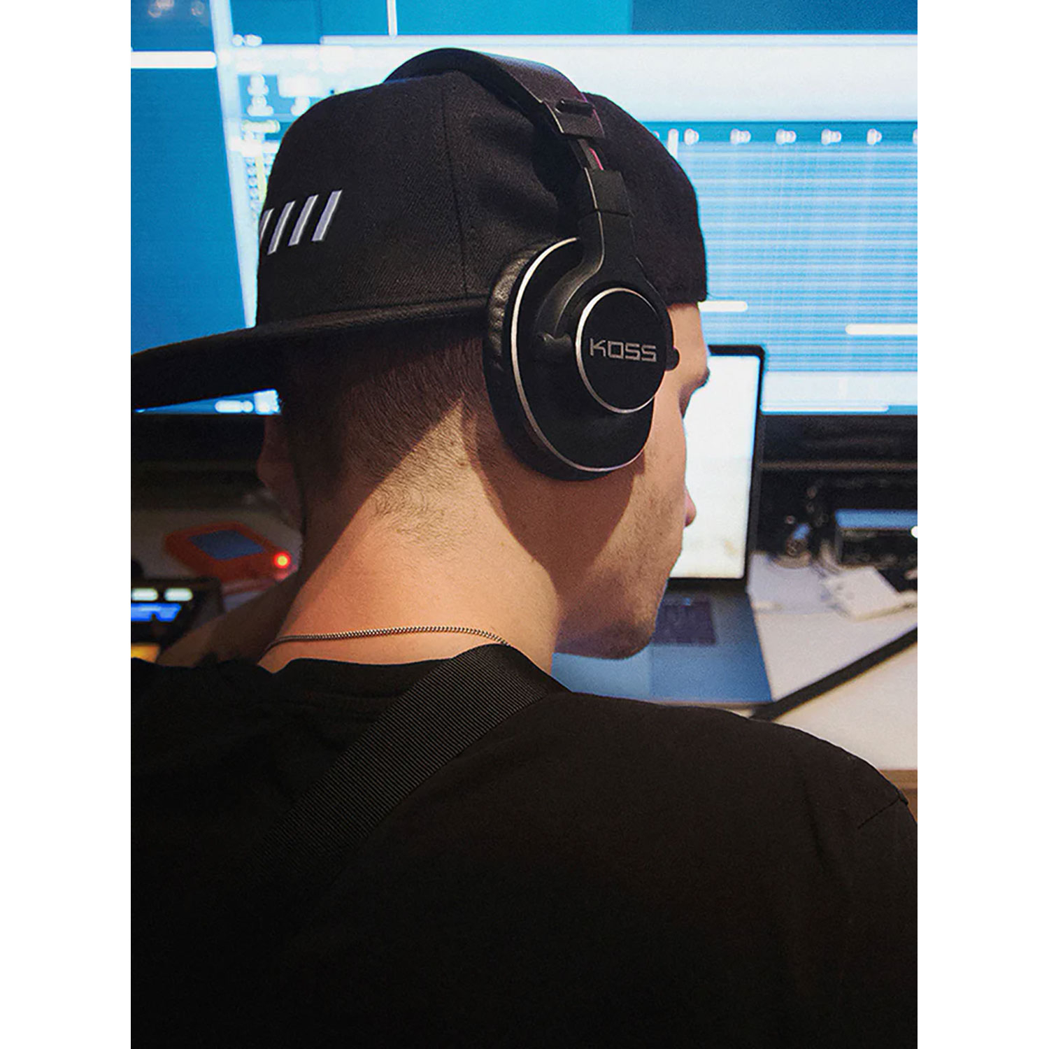 Mężczyzna w czapce i słuchawkach. Patrzy na ekran komputera. Niebieskie tło.