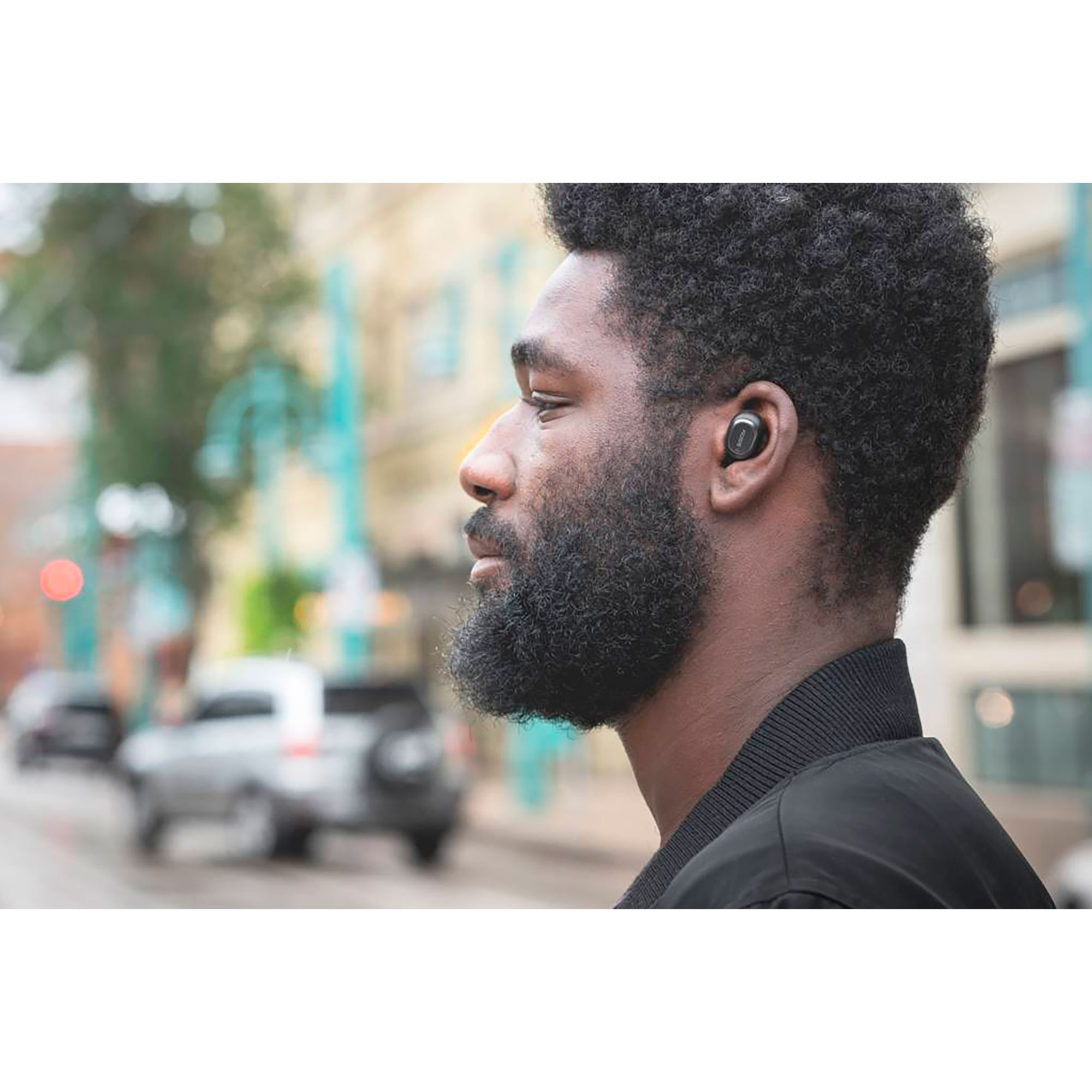 Un uomo con la barba indossa auricolari. È in una strada cittadina.