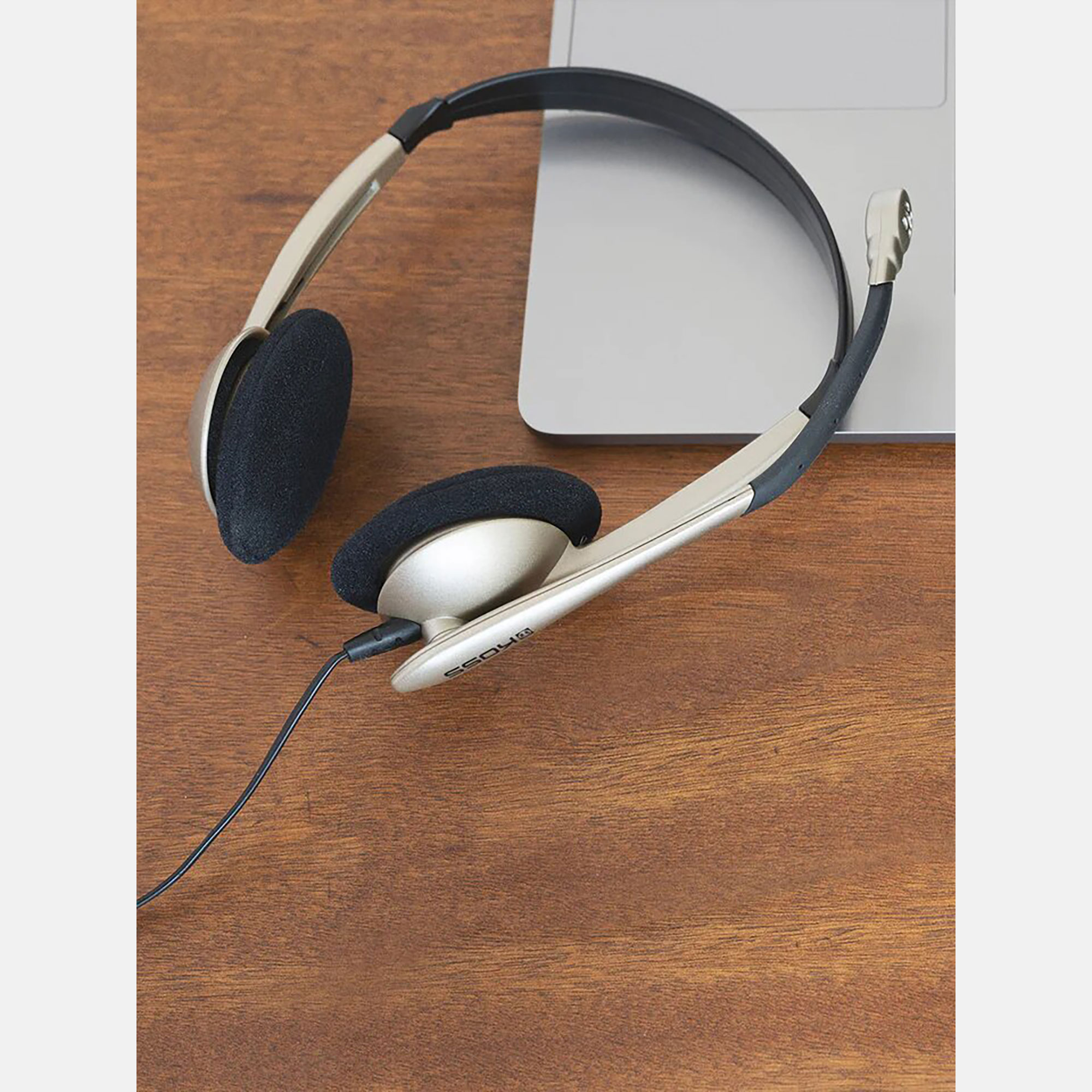Auriculares sobre una mesa de madera con un portátil al fondo.