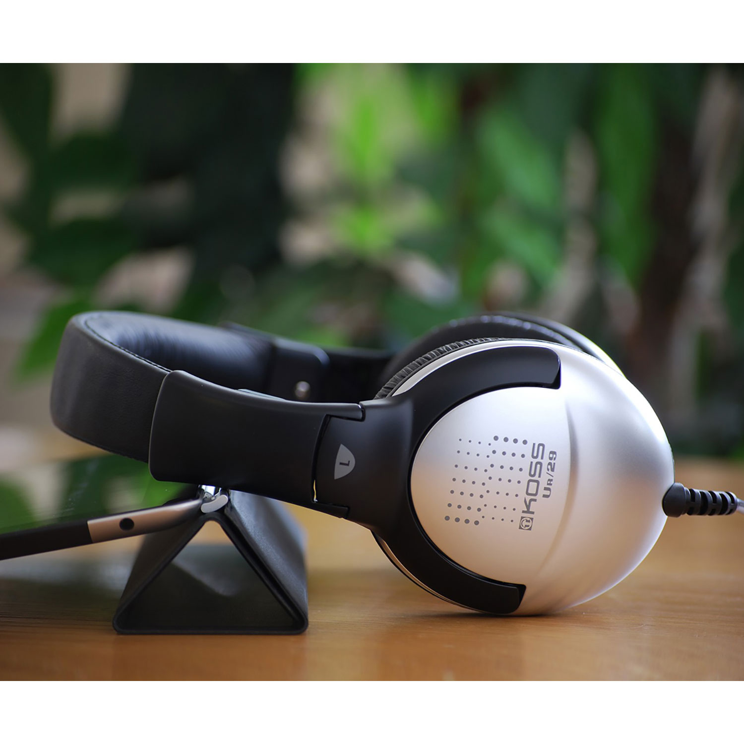 Srebrne słuchawki na stojaku. Czarny tablet po lewej. Drewniana powierzchnia.