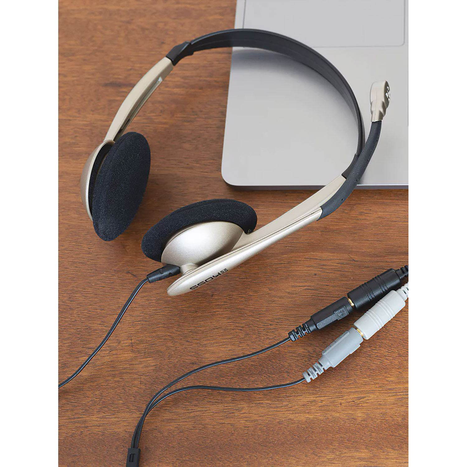 Cuffie su una superficie di legno accanto a un laptop e cavi audio.