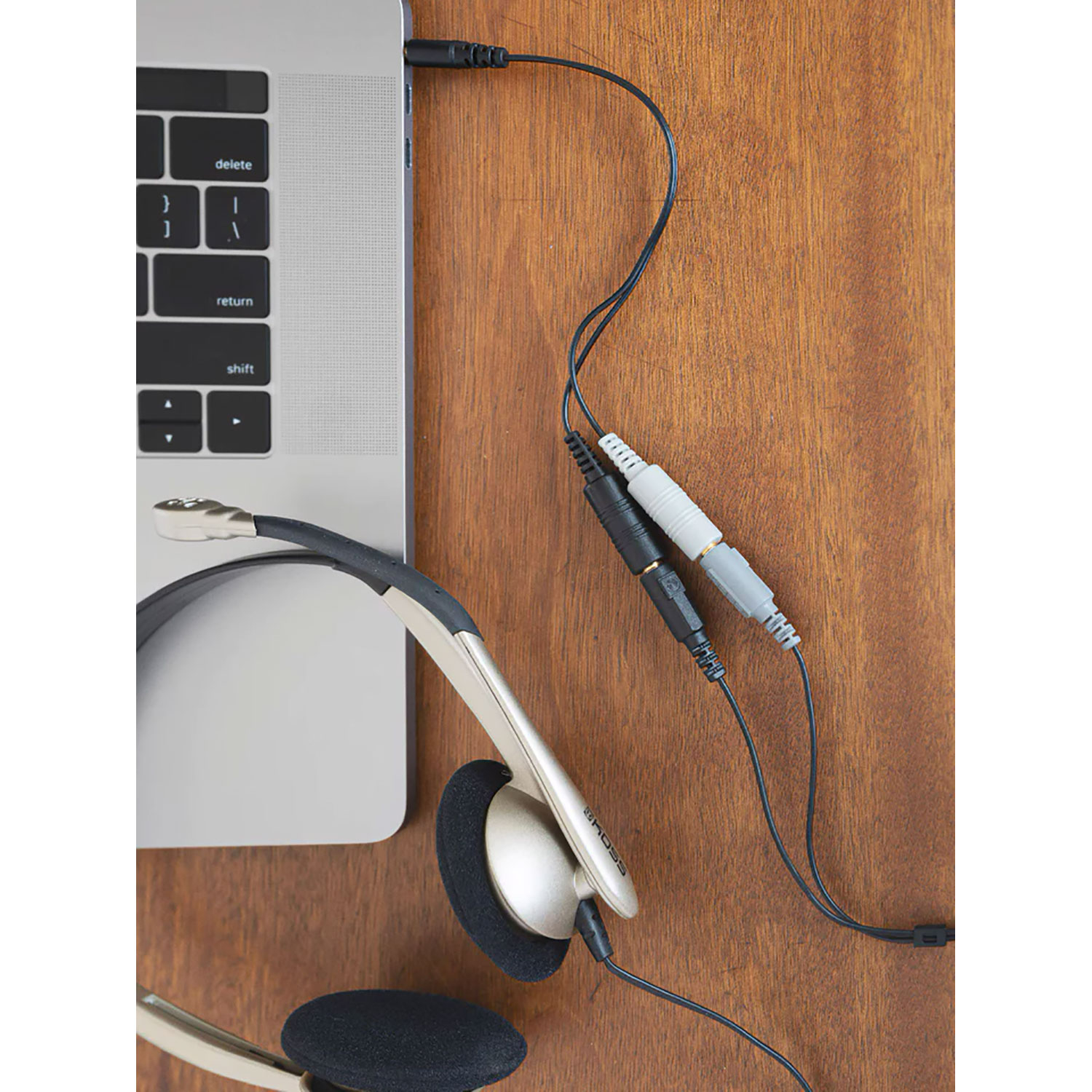 Una cuffia argentata collegata a un laptop. Cavi bianchi e neri si collegano alle porte audio.