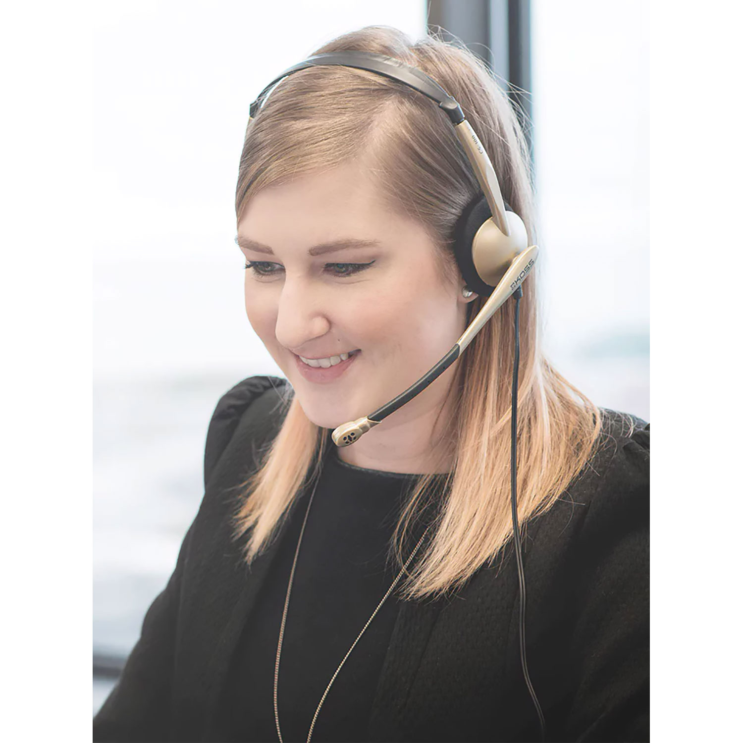 Eine Frau mit Headset lächelt, während sie auf einen Computerbildschirm schaut.