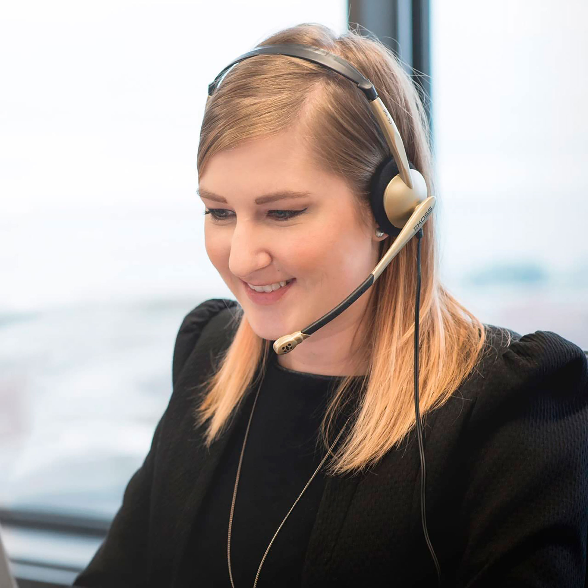 Mujer con auriculares sonriendo, con una ventana al fondo.